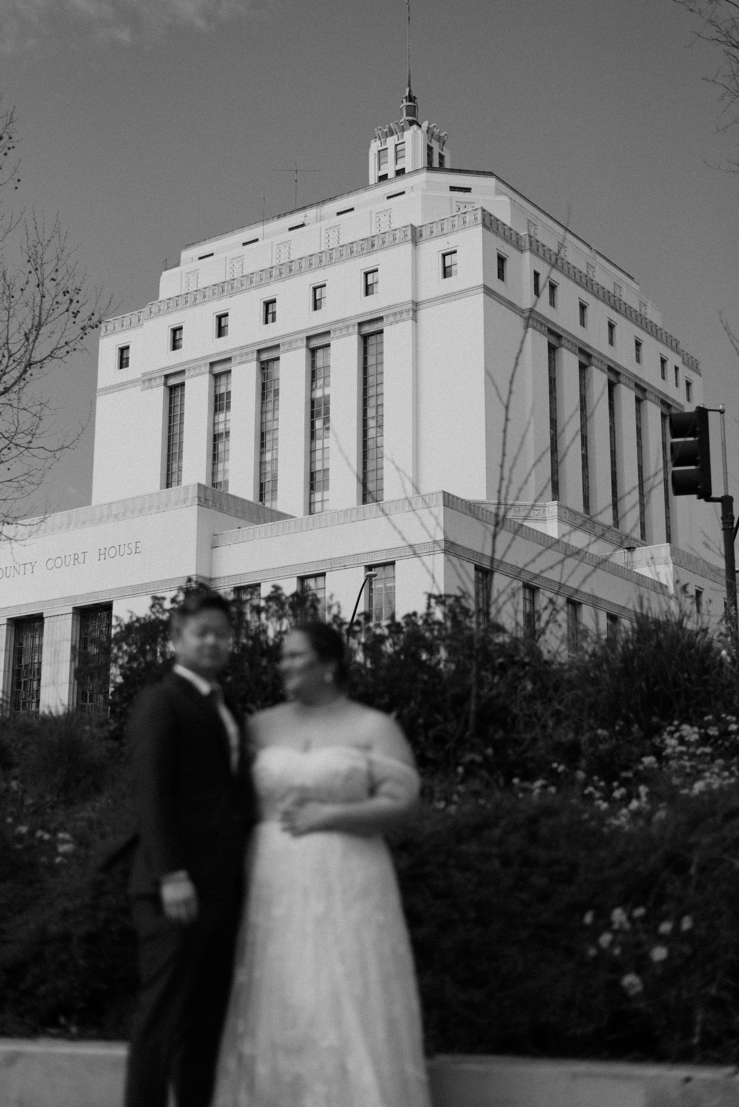 A wedding couple poses in front of a grand art deco courthouse building.