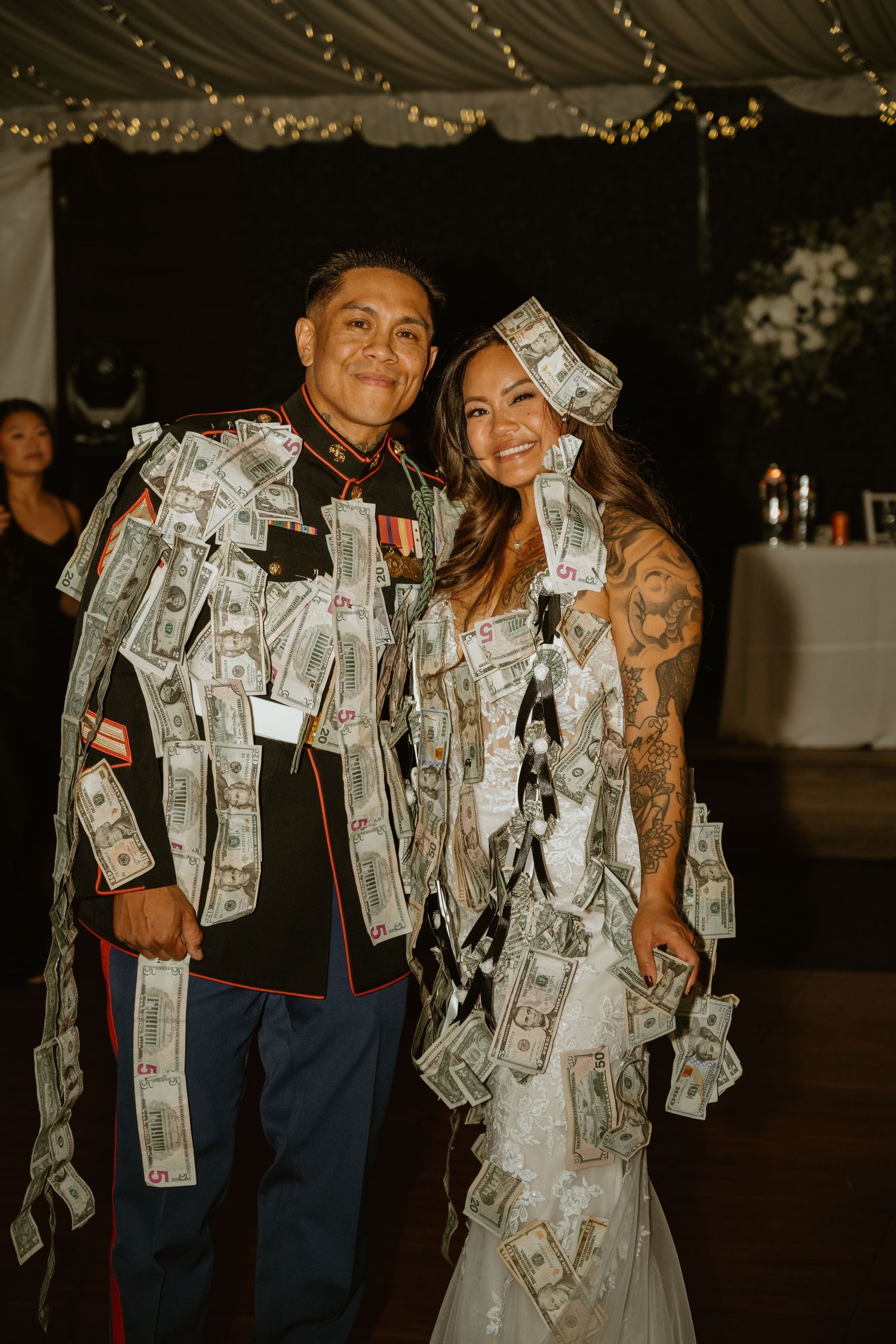 Wedding couple celebrating with dollar bills pinned to wedding attire during reception festivities.