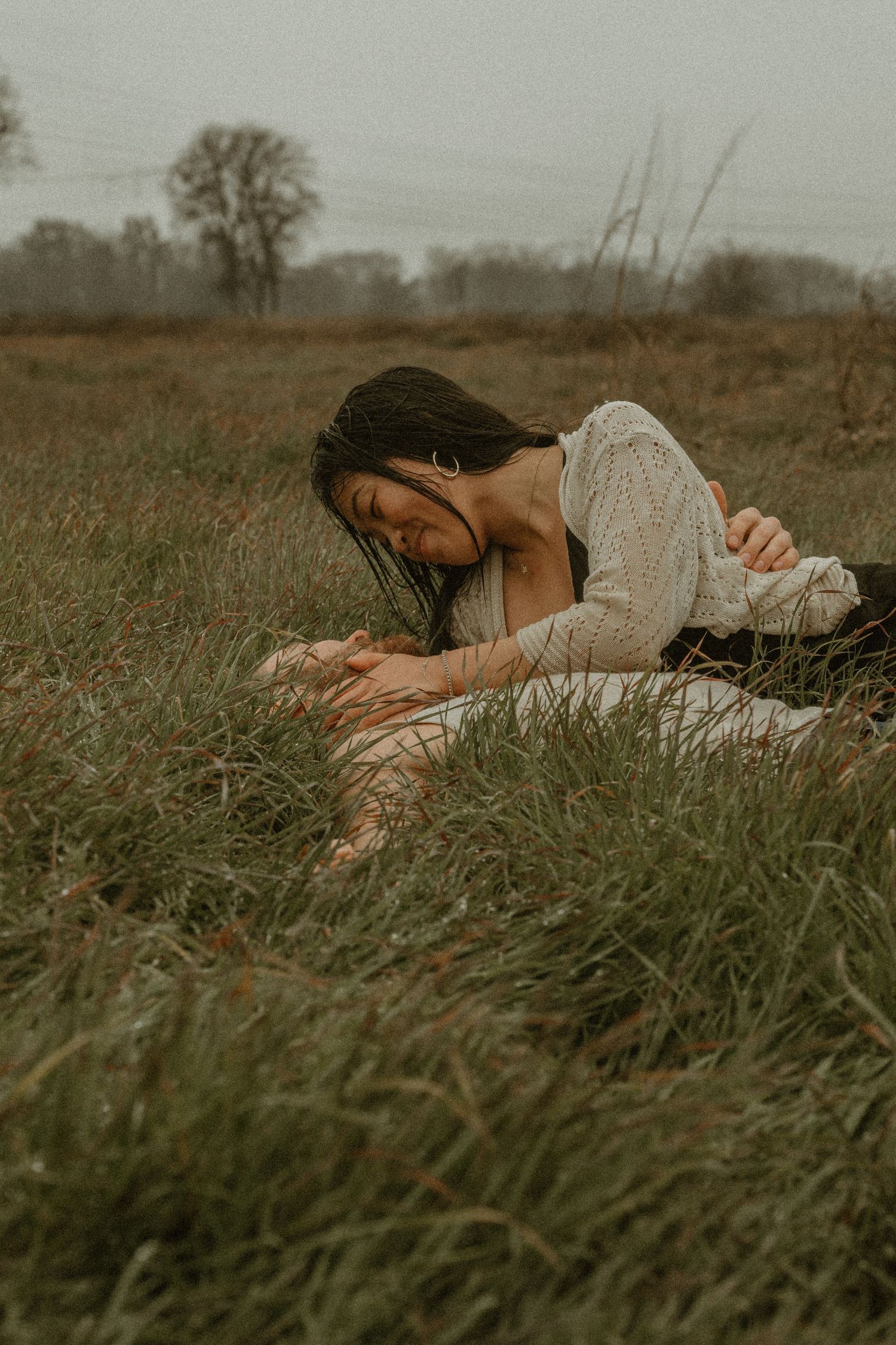 Person in gray sweater lying down in tall grass during golden hour.