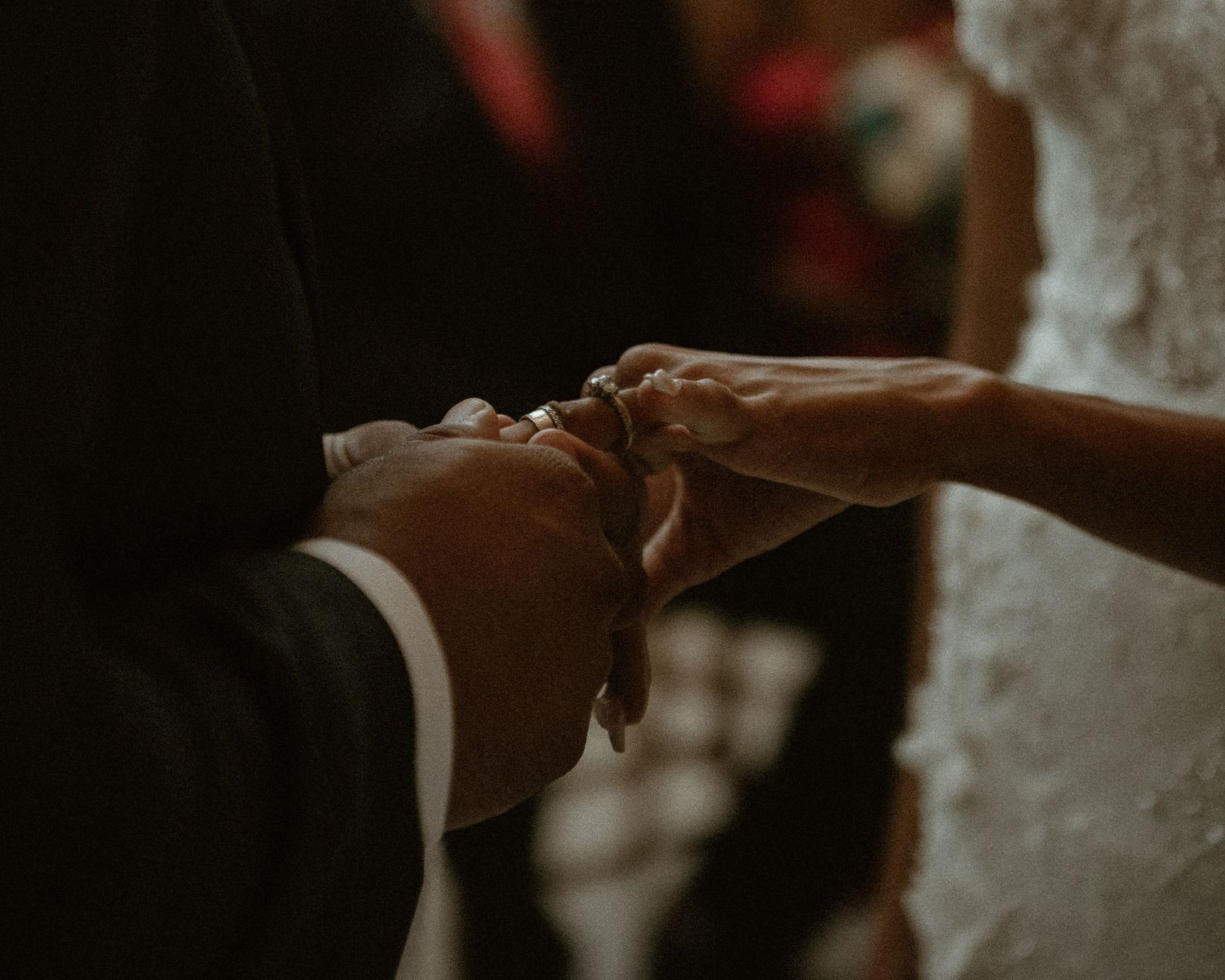 Close-up shot of hands touching during a wedding ceremony in warm, moody lighting.