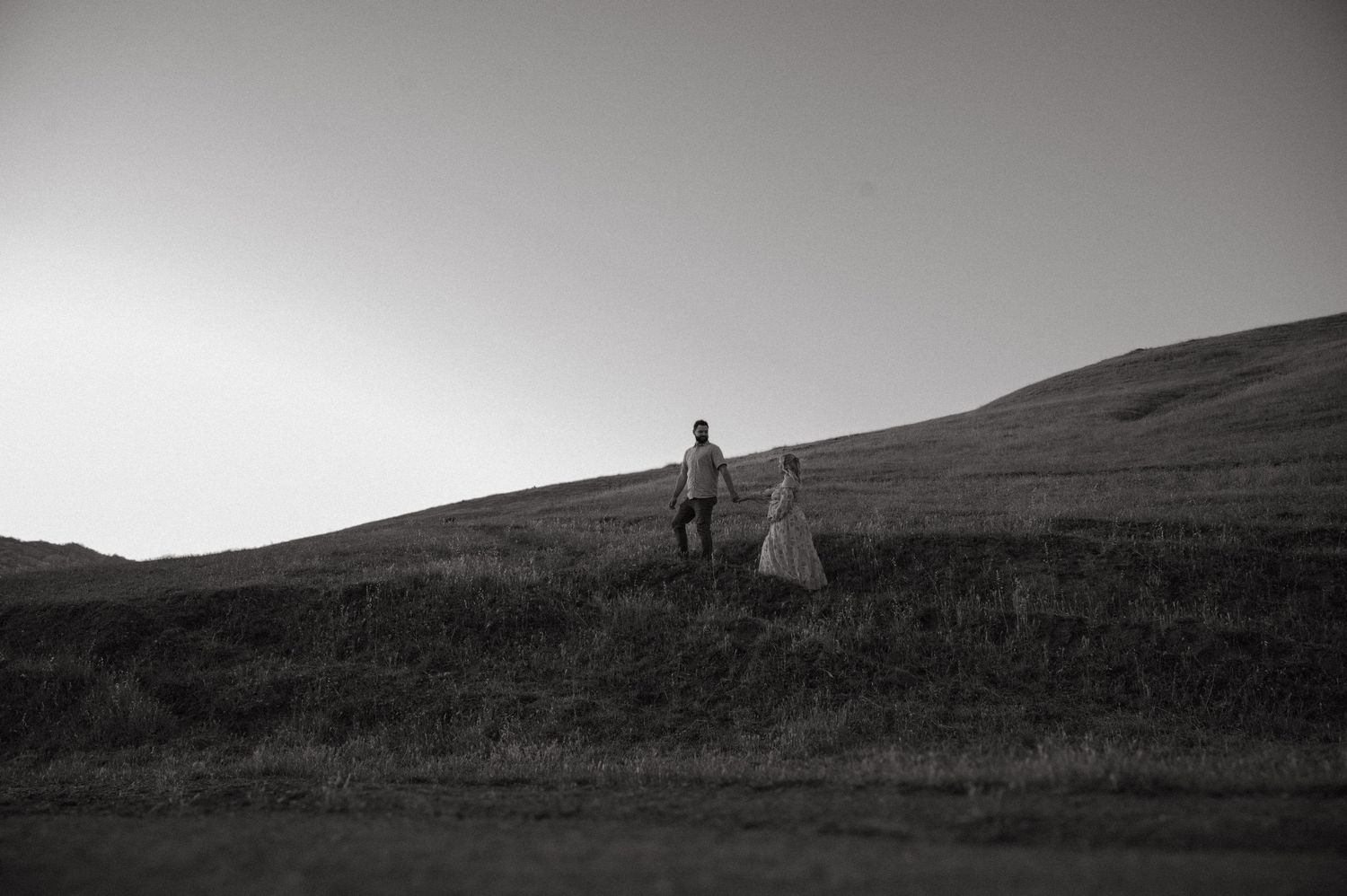 Silhouetted couple walking along hillside ridge in black and white.