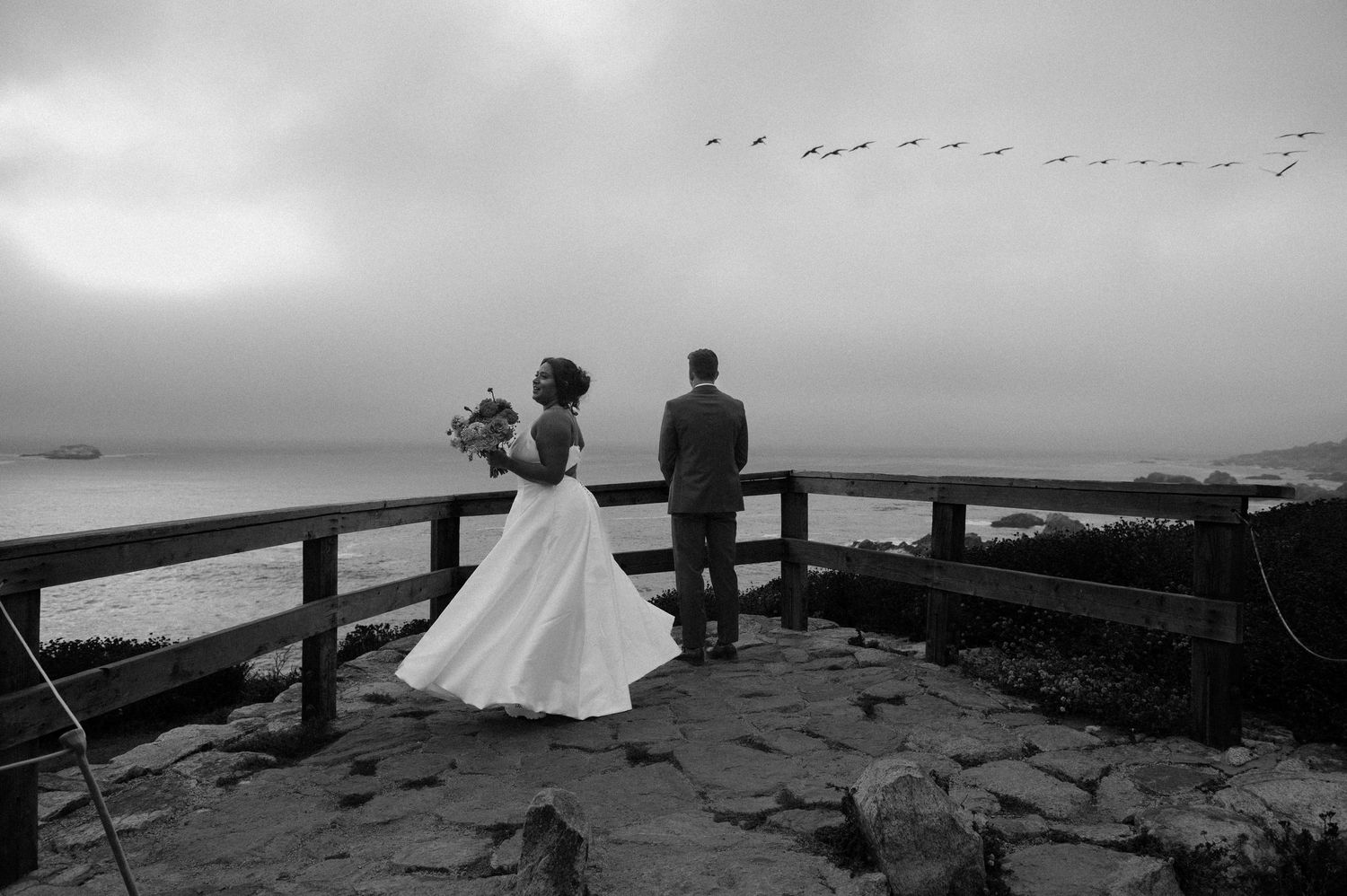 Silhouetted figures sit along rocky coastline during misty sunset.