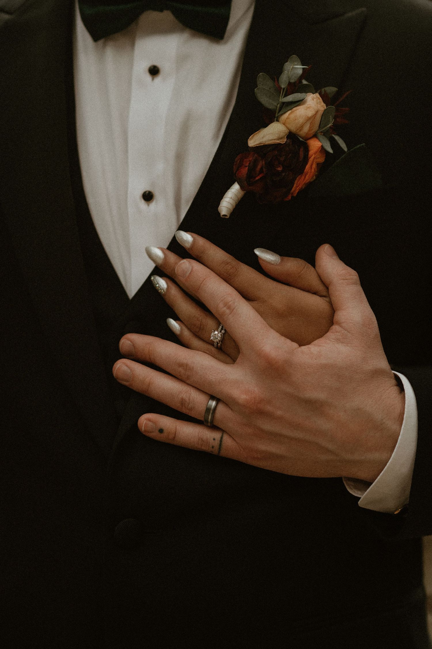 Close-up view of hands wearing wedding rings against a dark background with white accents.