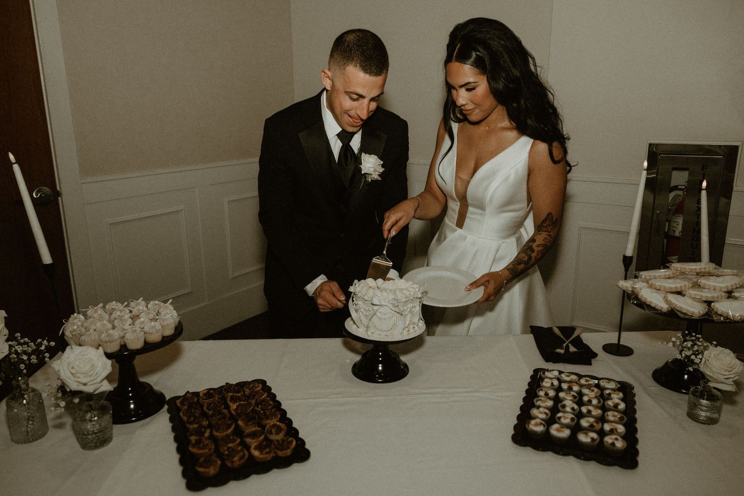 Newlyweds cut their elegant white wedding cake together at their reception dessert table.