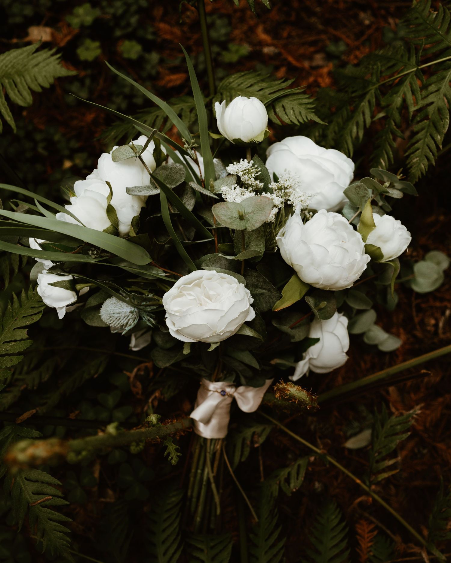 White peonies and delicate greenery create a romantic garden-inspired floral arrangement against a dark background.