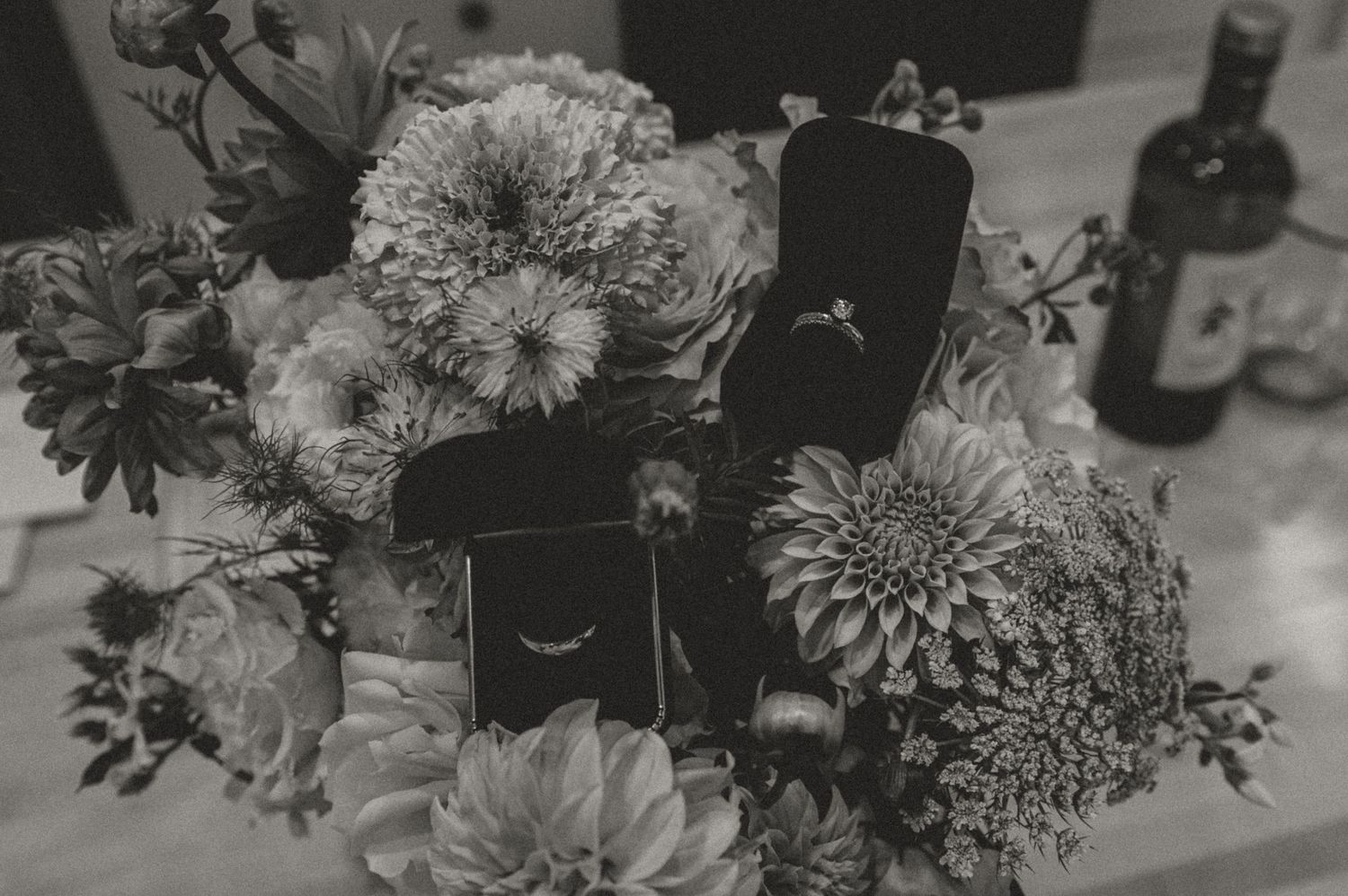 Wedding rings displayed in black boxes among fresh floral arrangements.