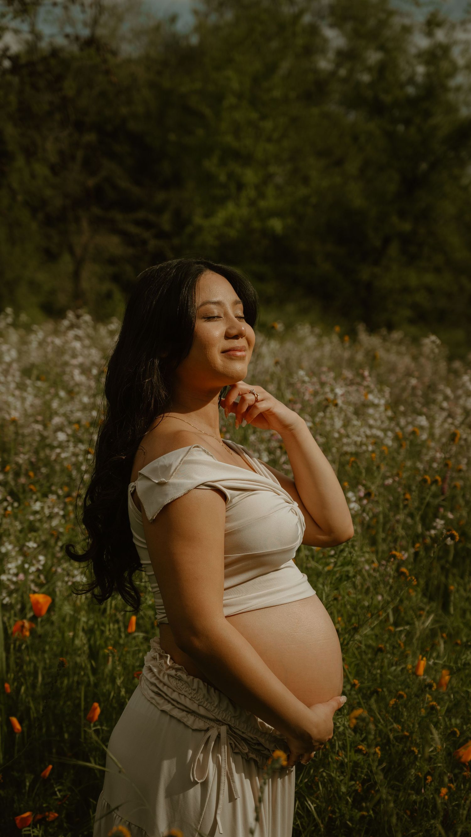 Dreamy maternity portrait in a field of wildflowers at sunset with orange poppies.