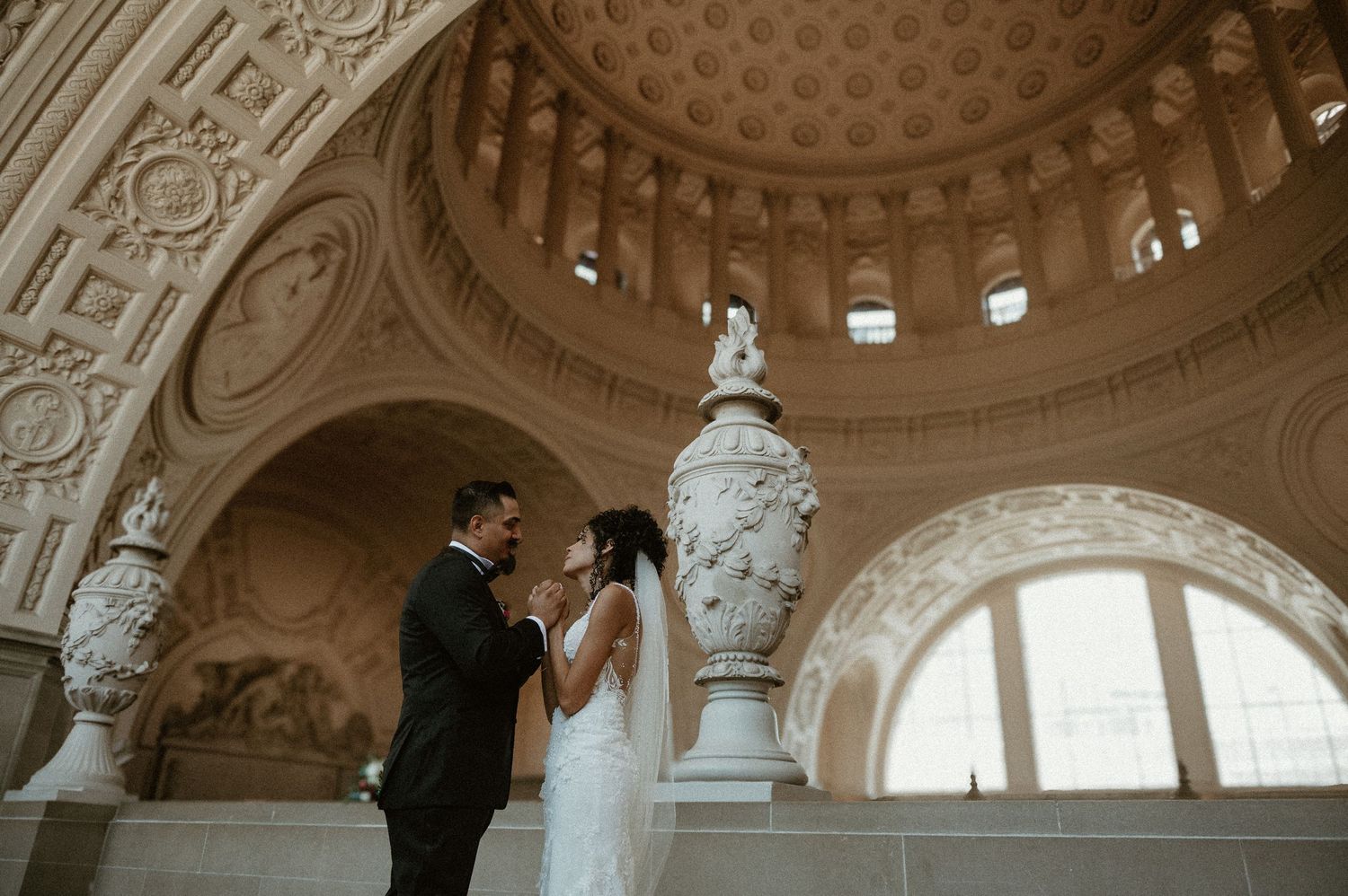 A couple shares an intimate moment under a domed ceiling with classical architectural details.