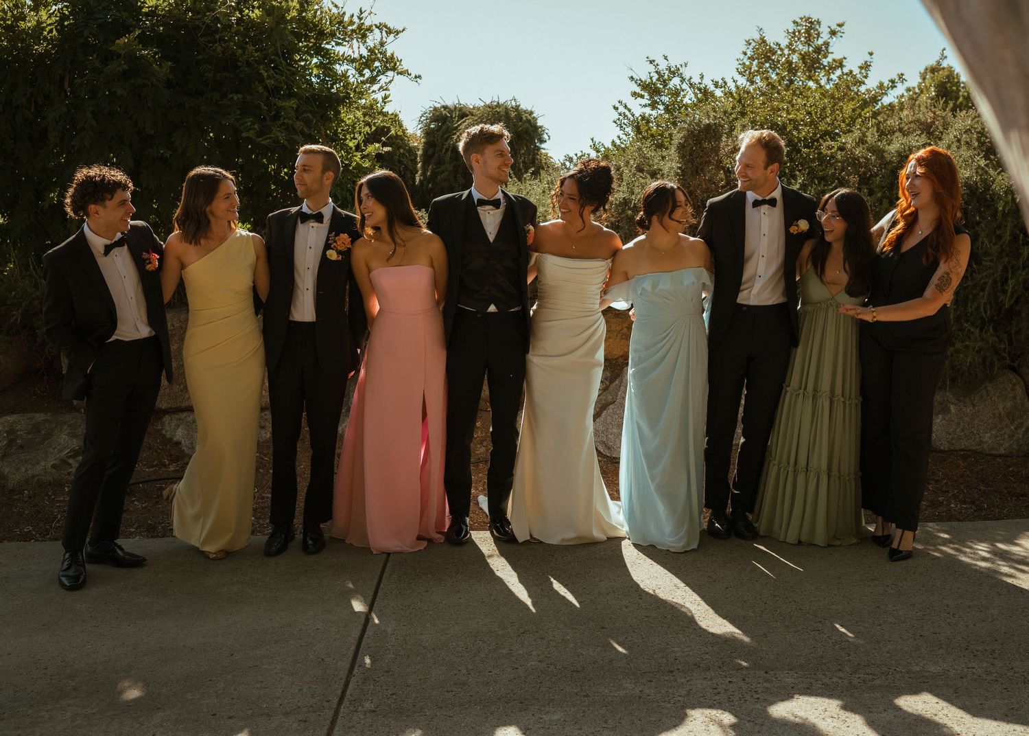 Wedding party in formal attire posing together in warm sunlight.