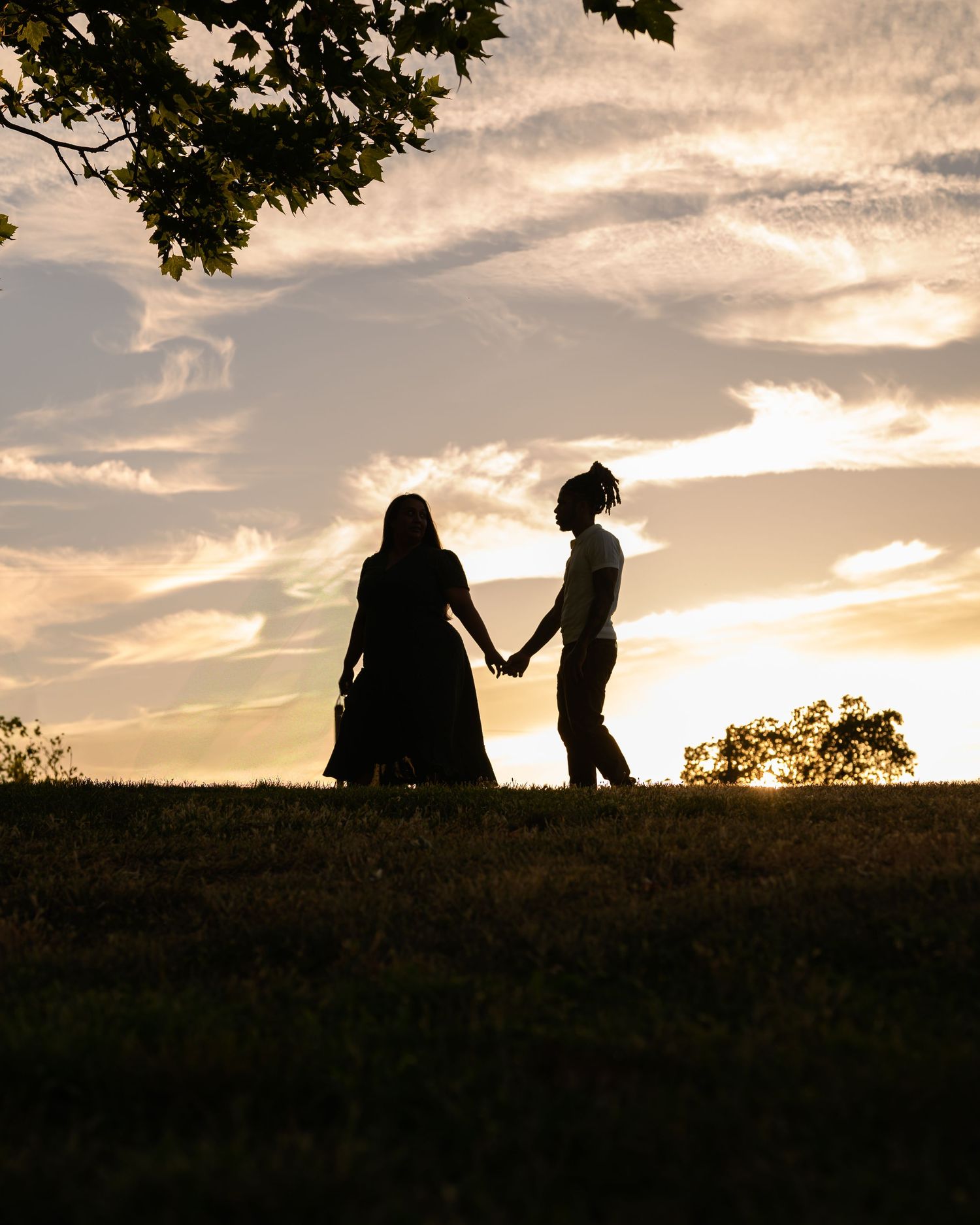 Silhouettes of couple against dramatic sunset sky under tree branches.