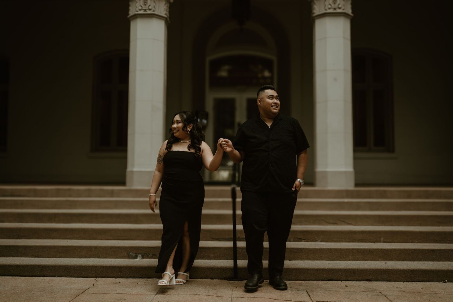 A couple stands together laughing on stone steps with classical columns in the background.