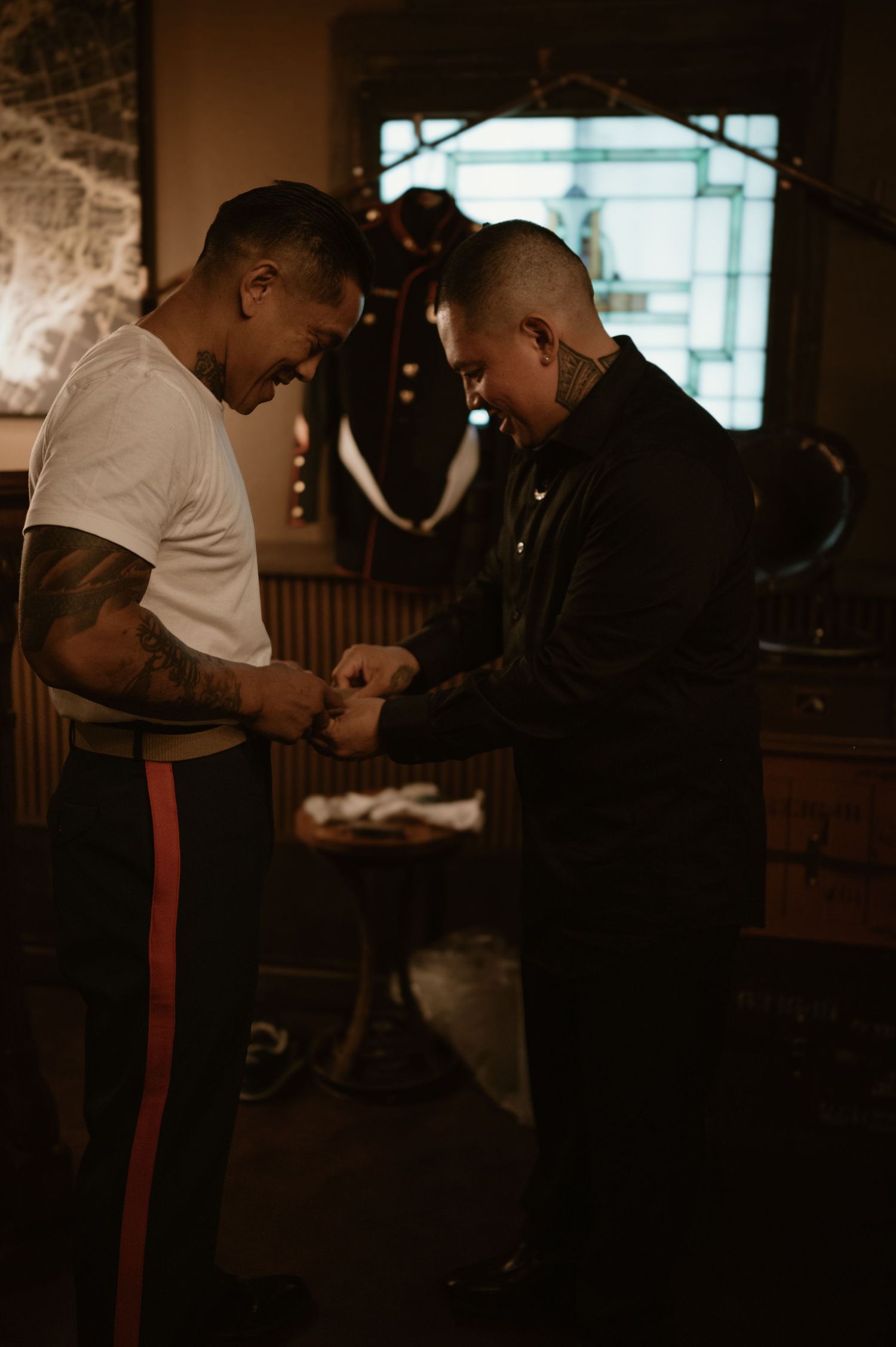 Two people examining something in a dimly lit room with moody lighting and stone walls.