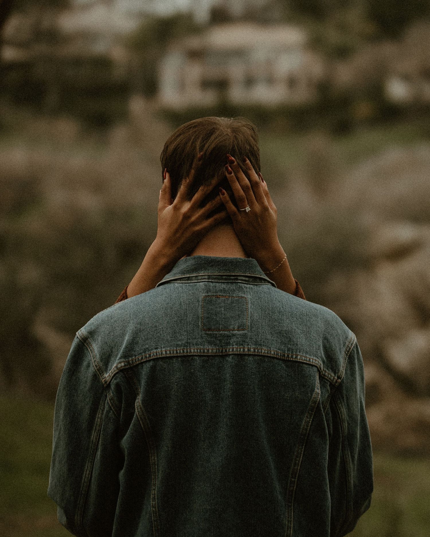 A person in a denim jacket shown from behind against a blurred natural background.