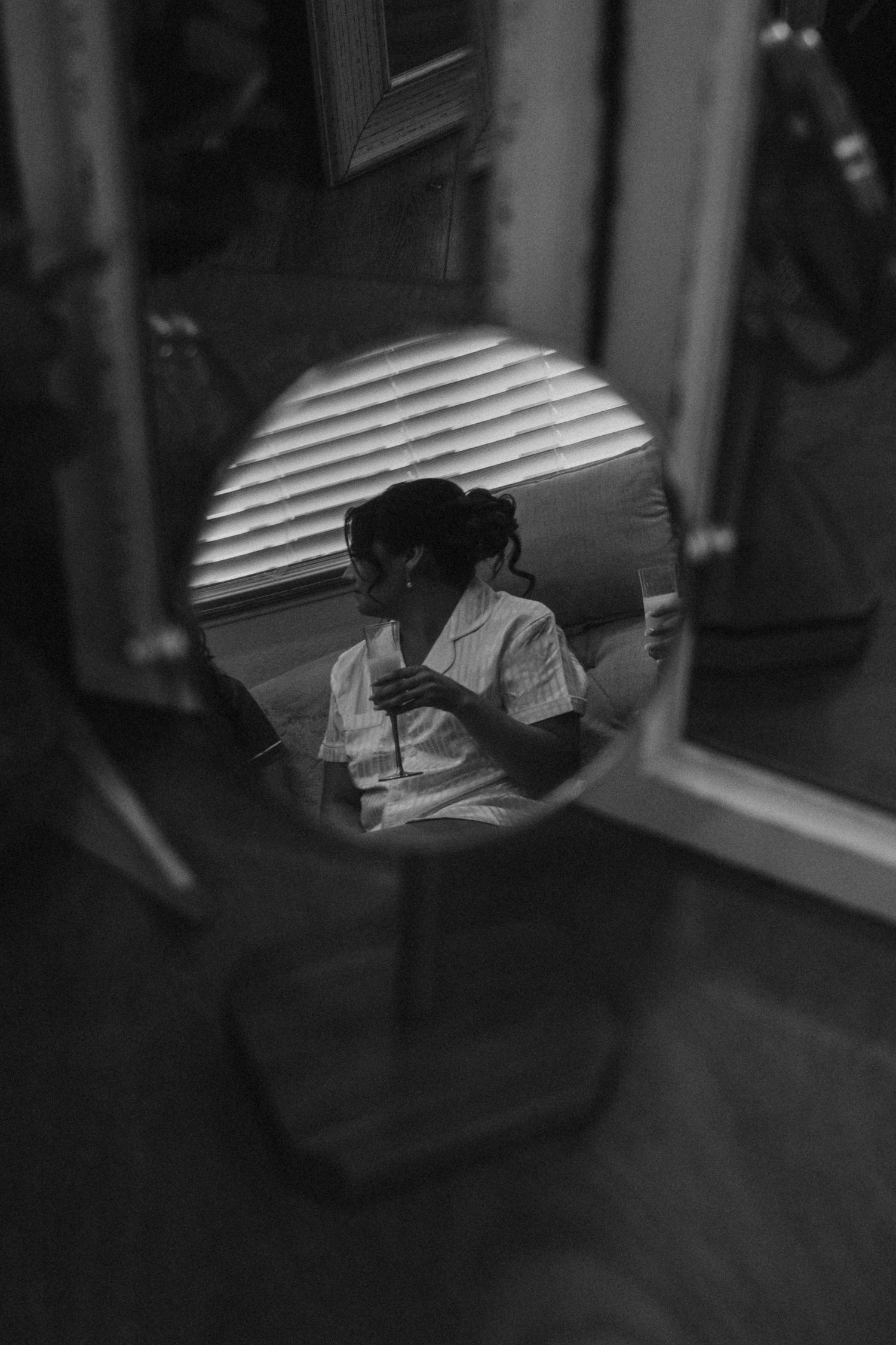 Artistic black and white reflection of a person in a circular mirror with venetian blind shadows.