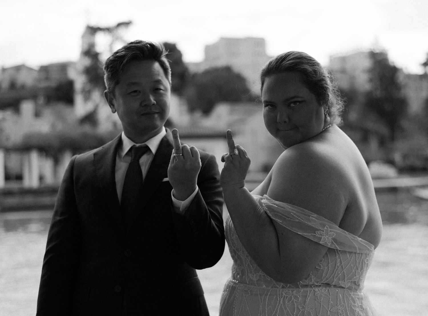 A couple shows their wedding rings to the camera in a candid black and white portrait.