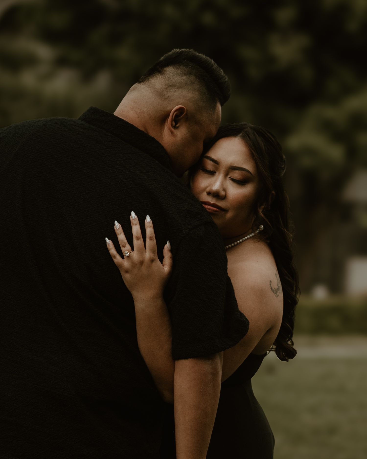 A tender embrace captured in moody lighting against an outdoor background.