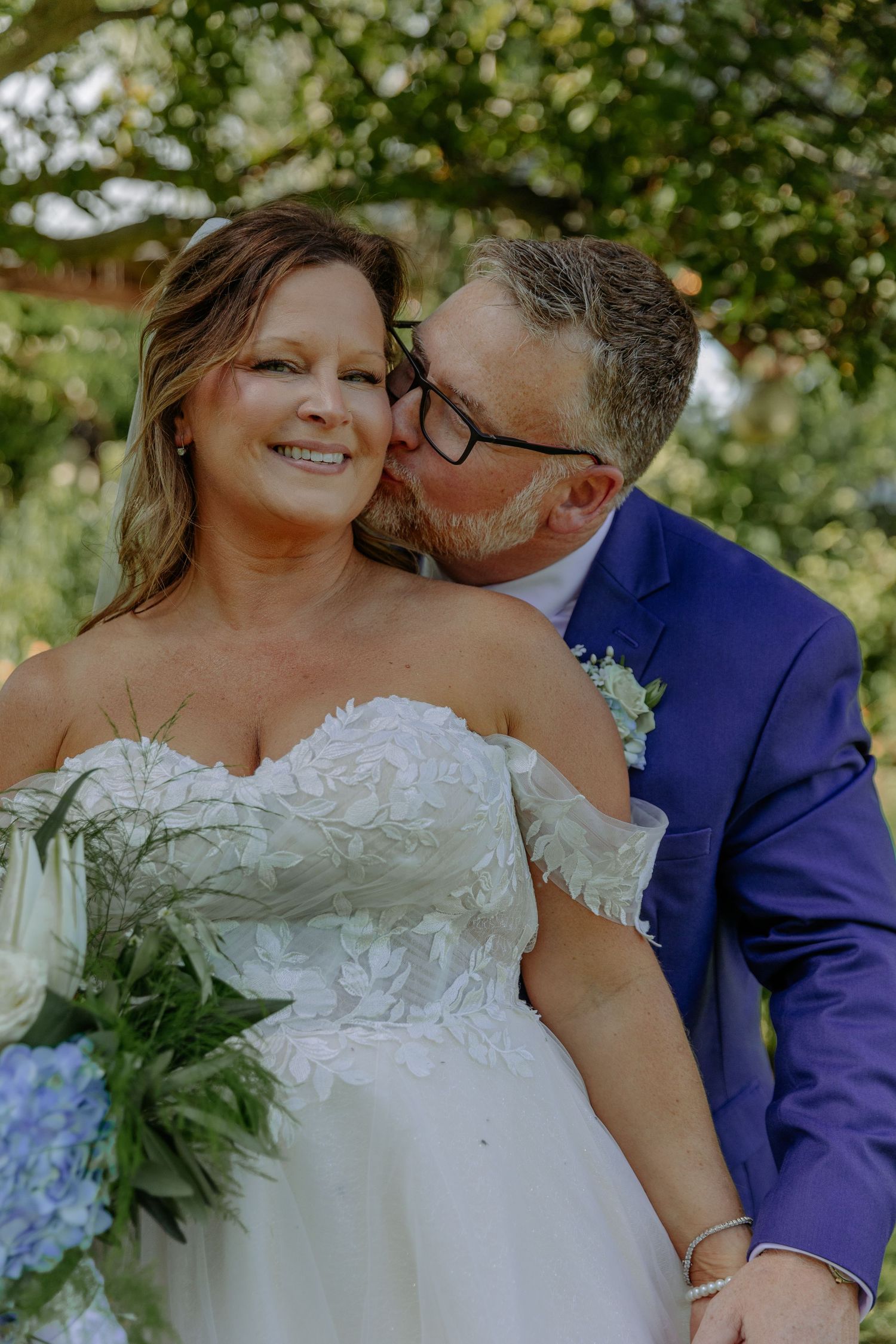 Sweet moment between newlyweds in garden setting with blue suit and white gown.