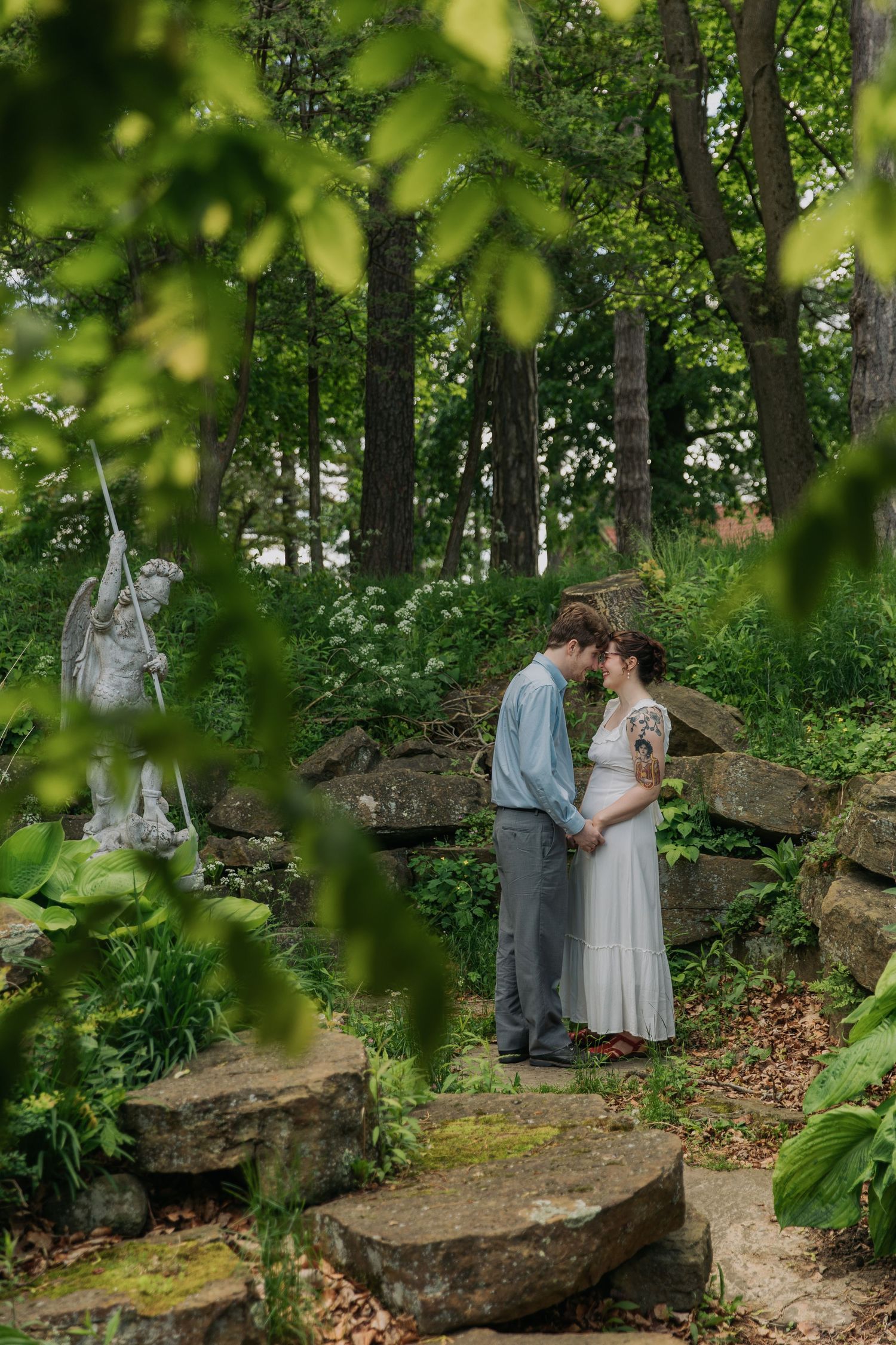 Couple having intimate wedding photos taken among moss-covered rocks in wooded setting.