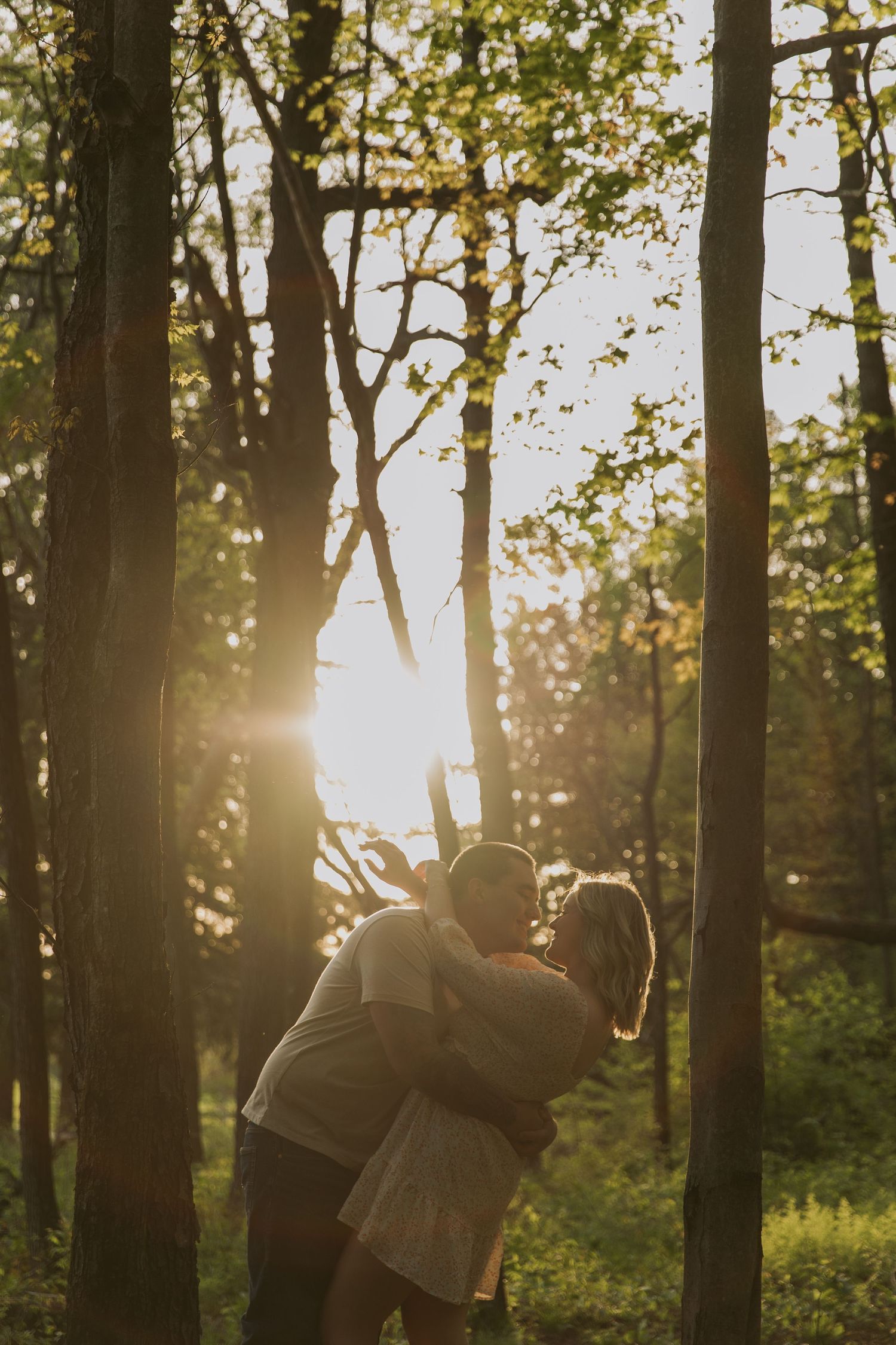 Silhouetted couple embracing in a forest during golden hour sunset.
