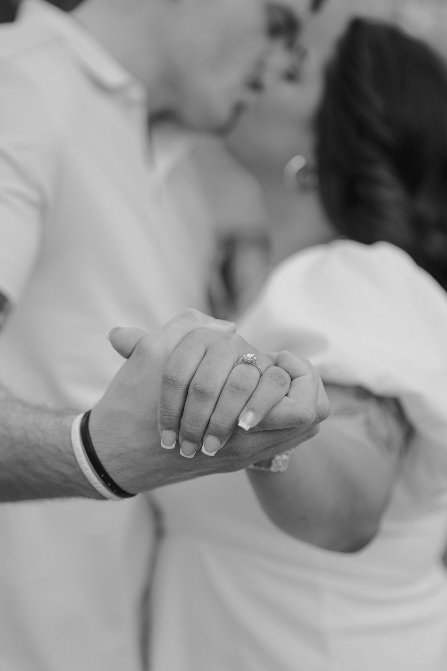 Close-up black and white photo of hands clasped together showing wedding rings.
