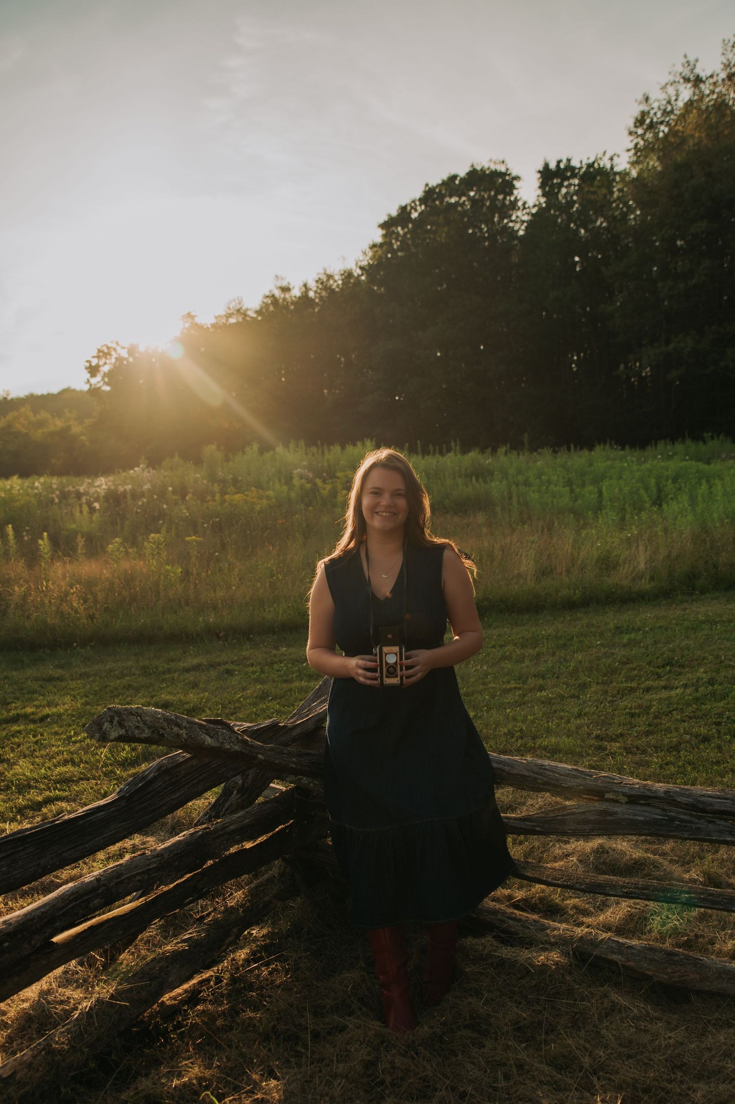 Photographer with vintage camera posing on wooden logs during golden hour sunset.