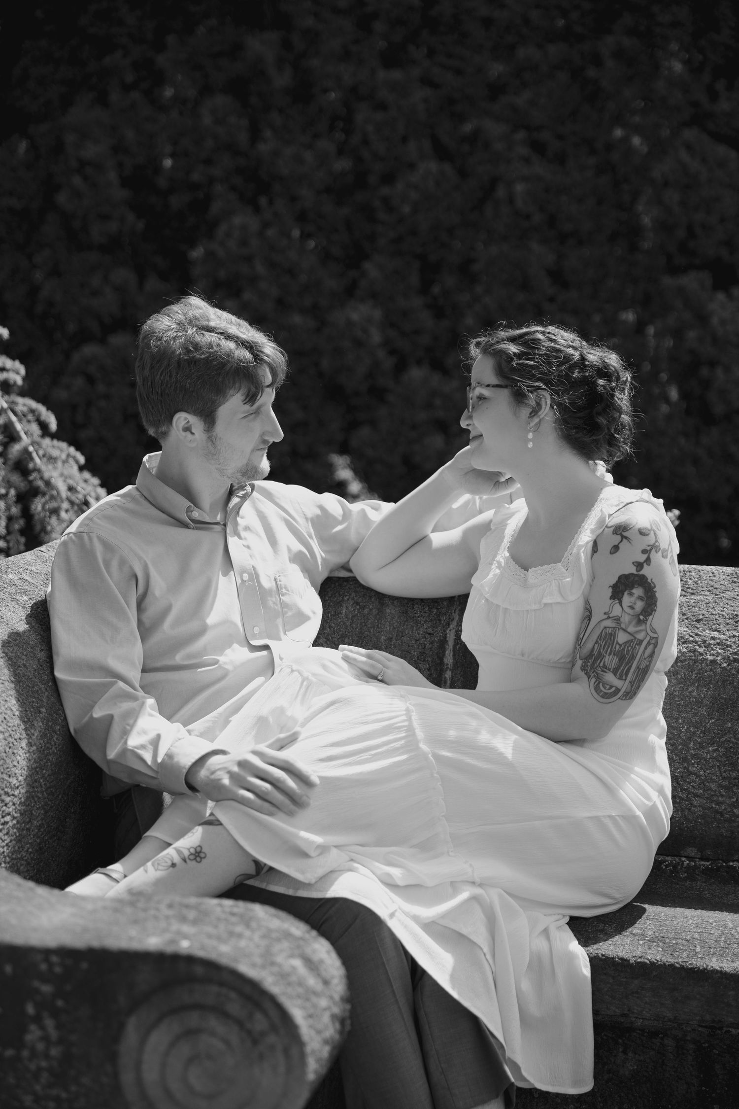 Black and white vintage-style romantic portrait on stone bench outdoors.