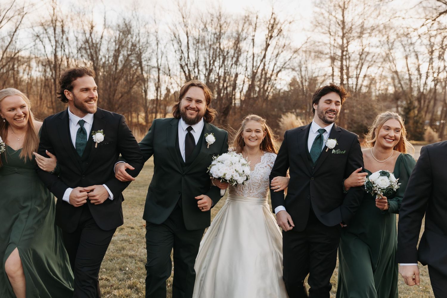 Wedding party laughs together while posing outdoors during golden hour in formal attire.