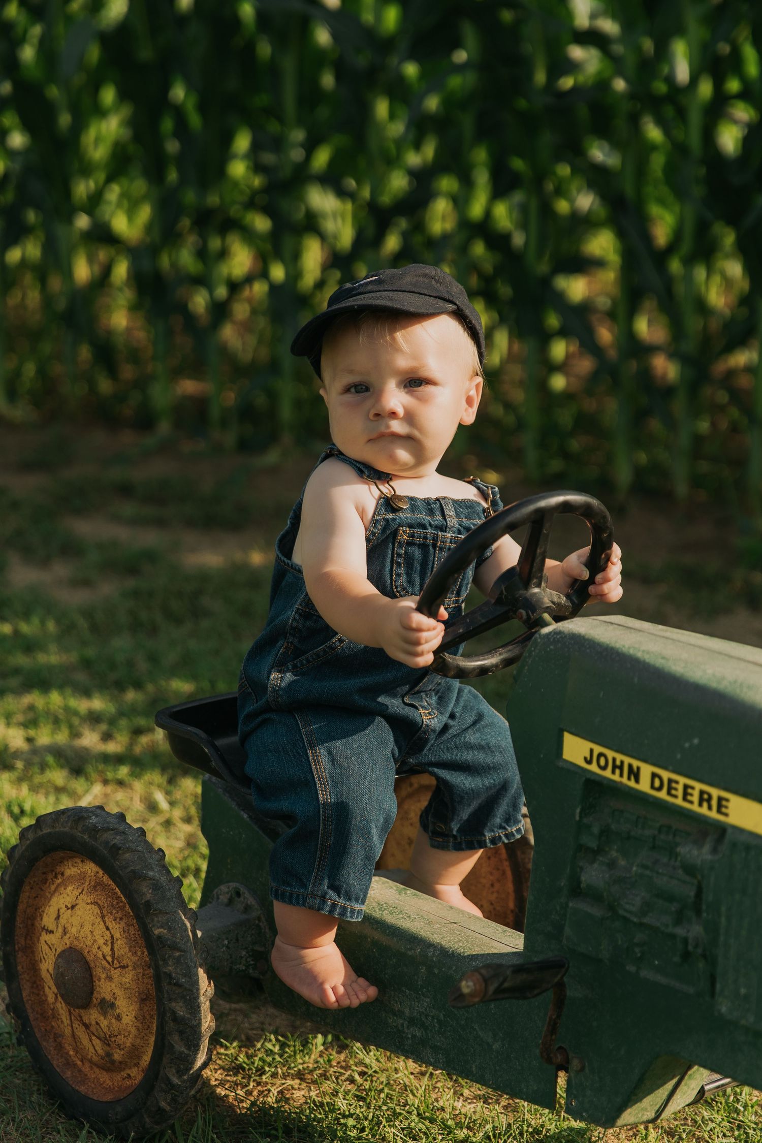 Small child playing on vintage John Deere toy tractor in garden setting.