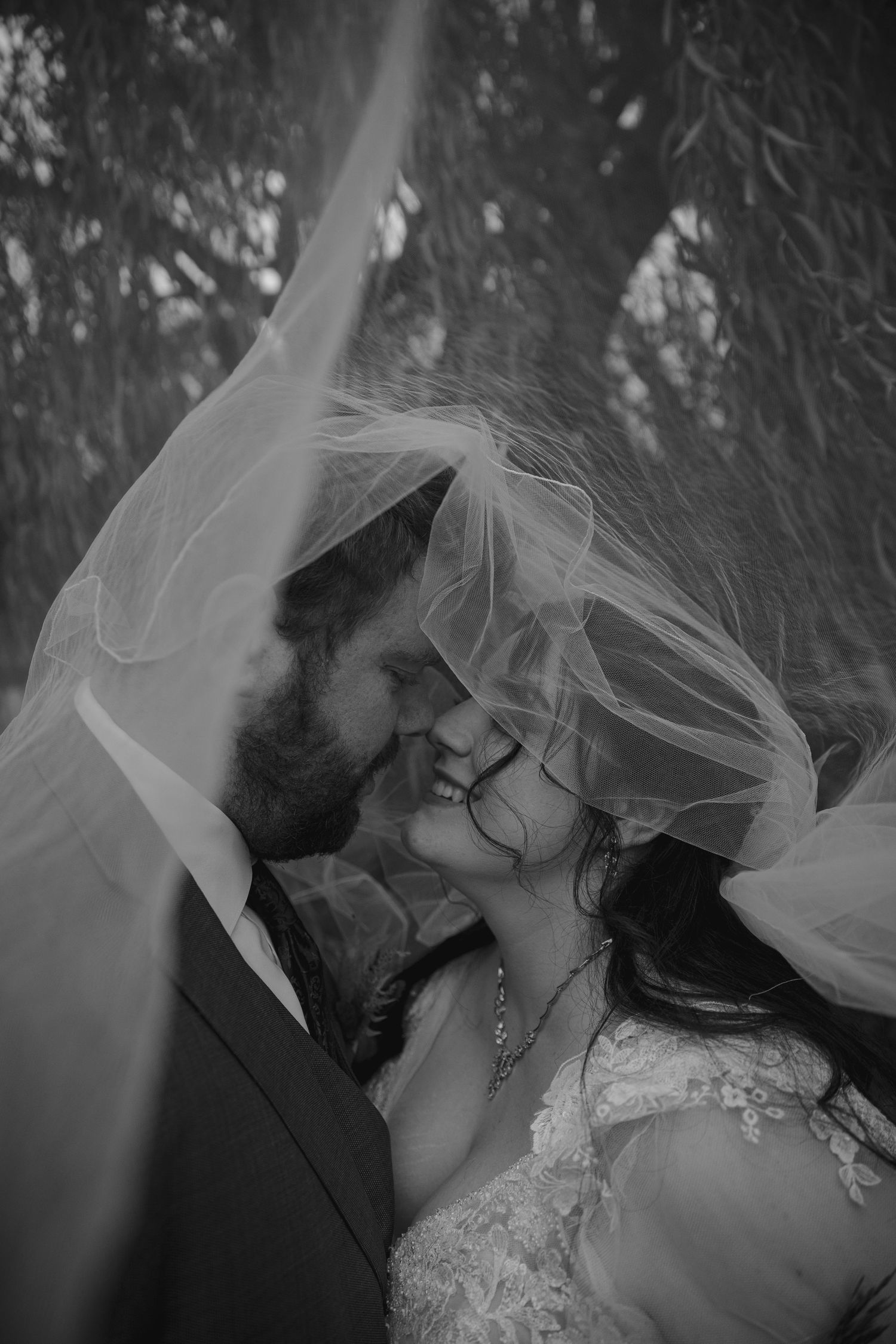 A romantic black and white portrait of newlyweds sharing an intimate moment under a flowing veil.