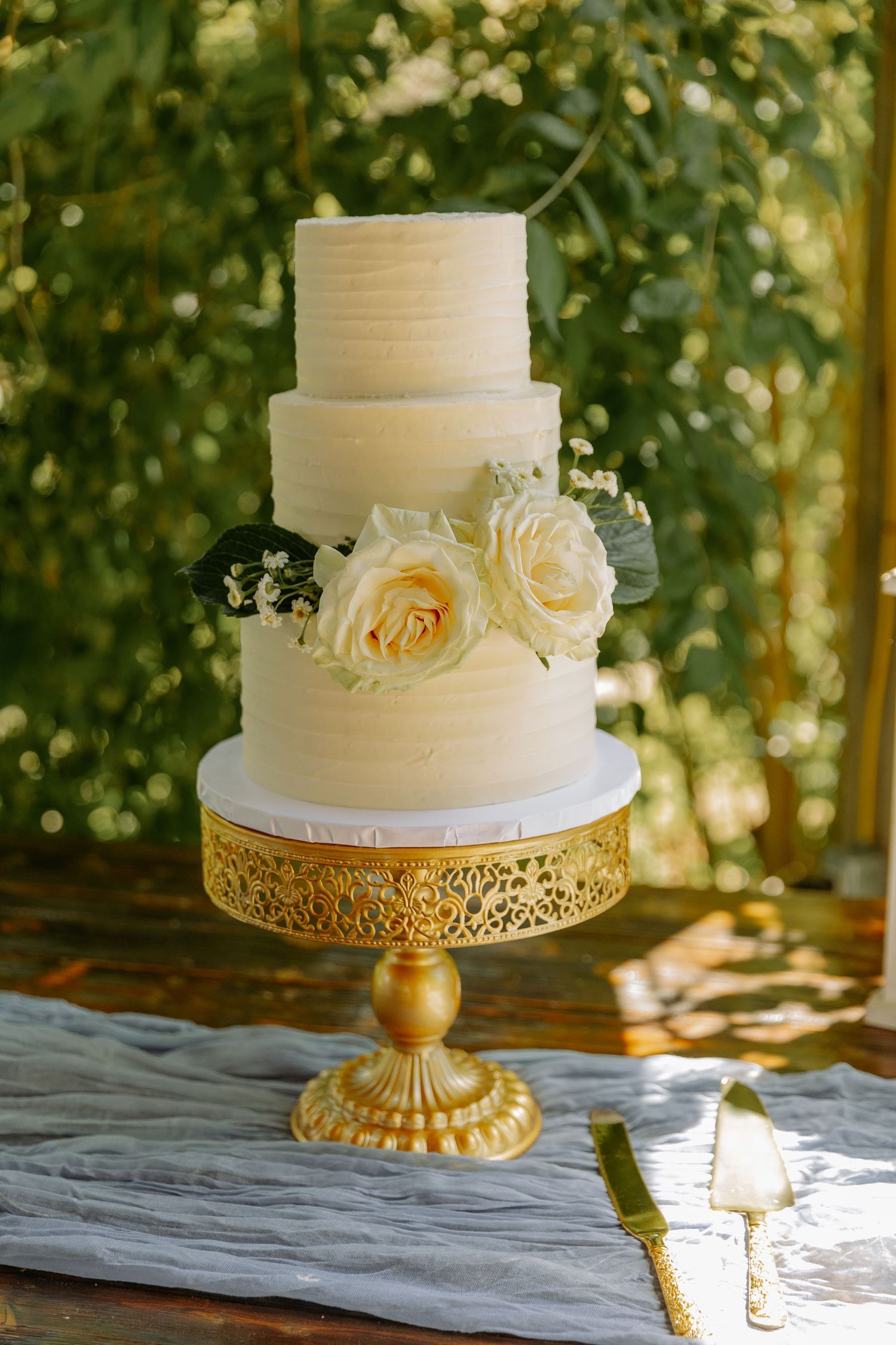 An elegant three-tier white wedding cake with fresh roses on a gold pedestal stand in Central Pennsylvania