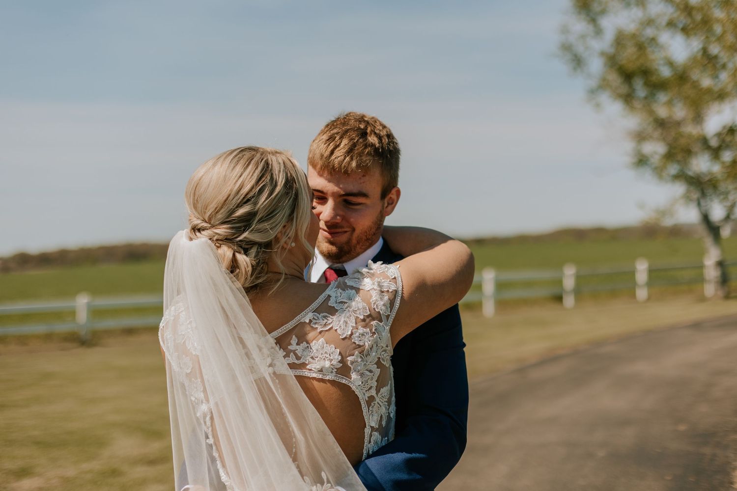 A romantic moment between newlyweds on a countryside path with white veil flowing in the breeze.
