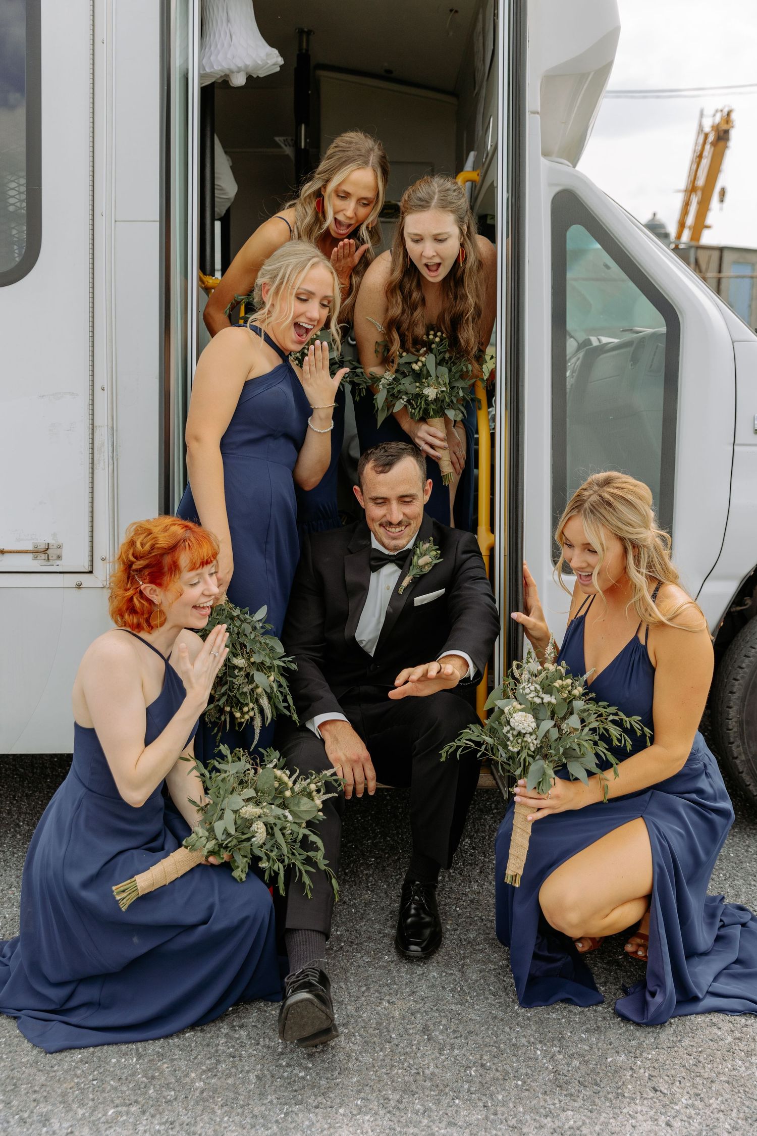 Bridesmaids in navy blue dresses share a fun moment together outside a wedding venue.