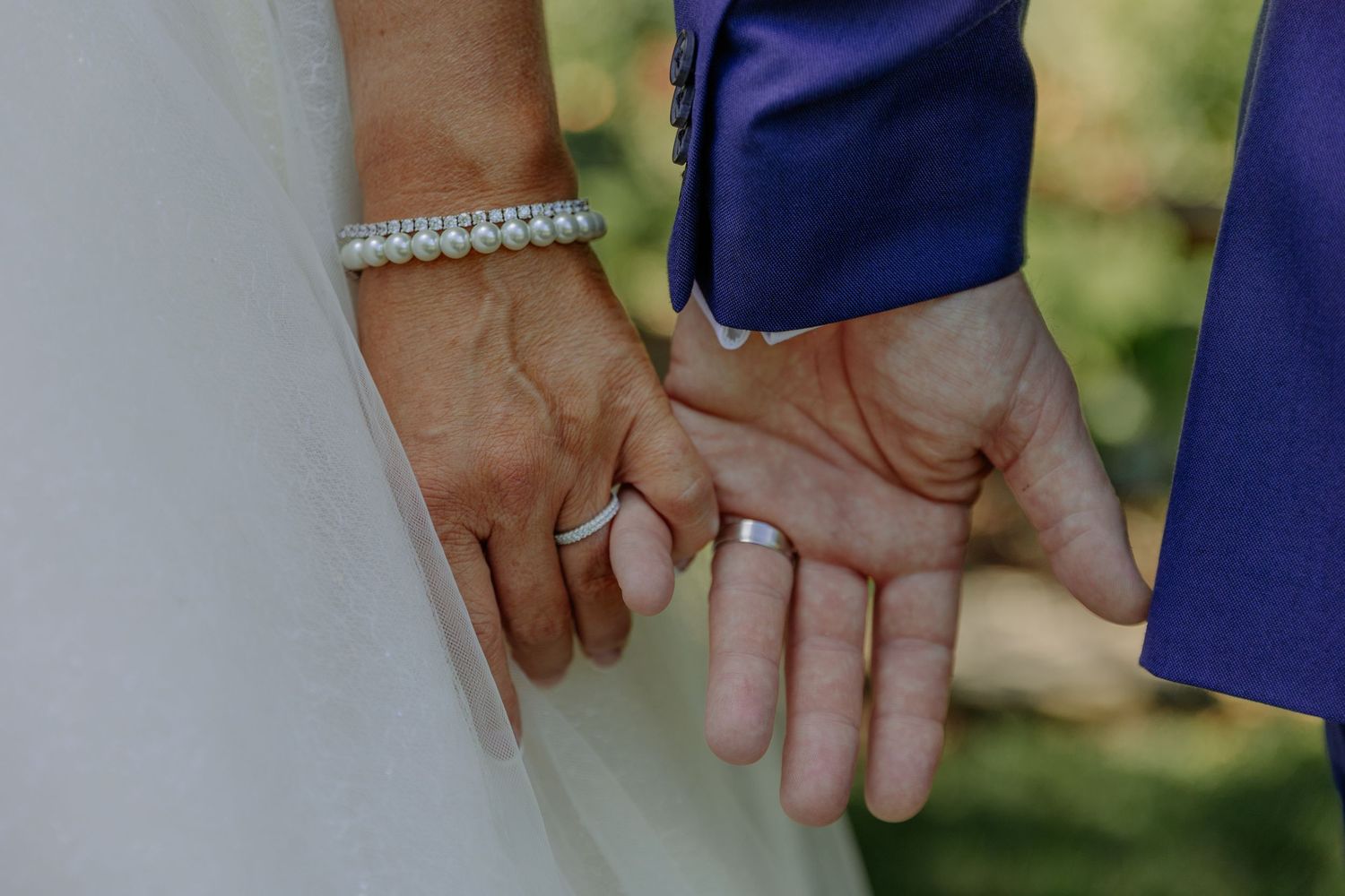 Close-up of hands wearing wedding rings and formal attire.