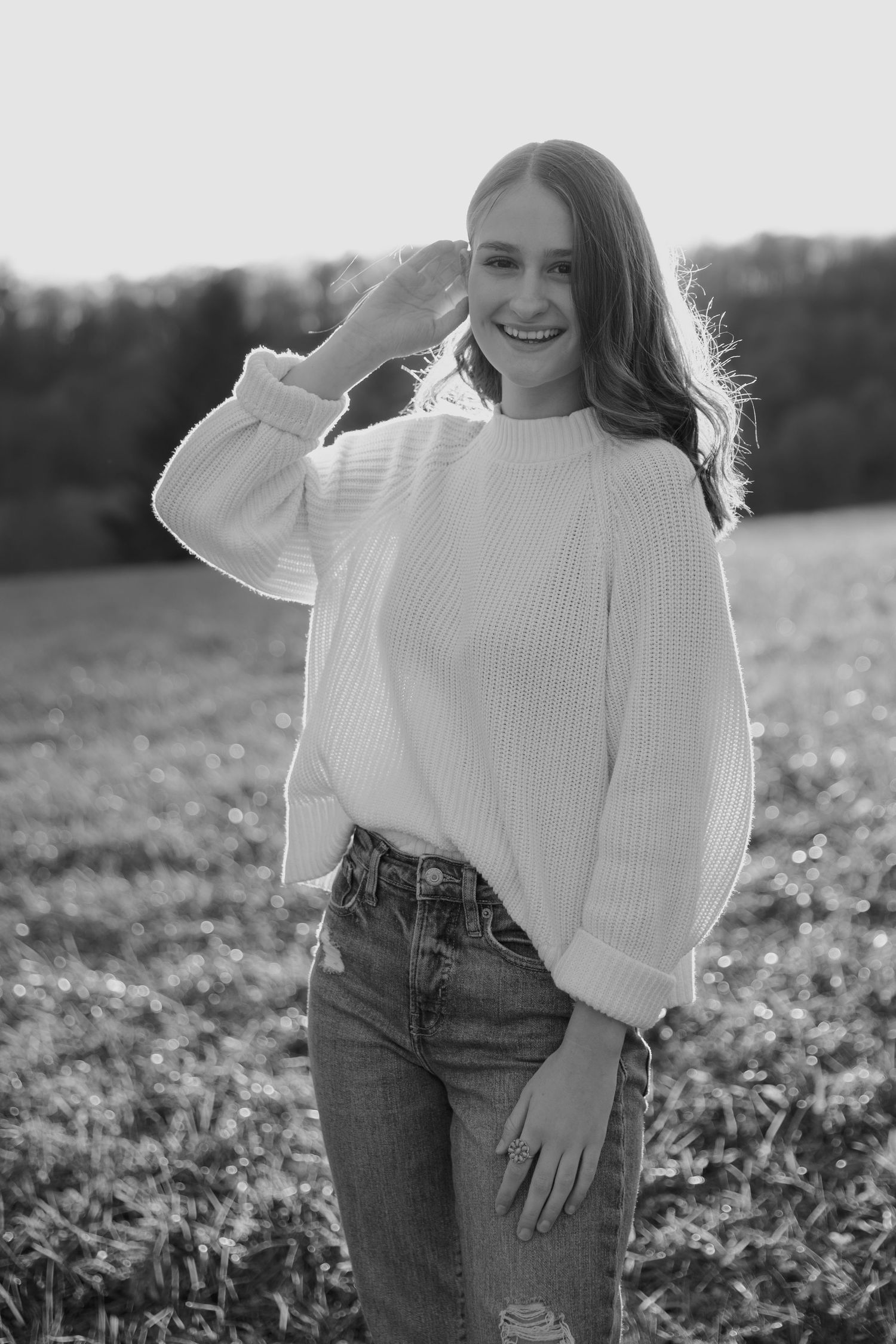 Person in white sweater and jeans posing in a sunlit field.