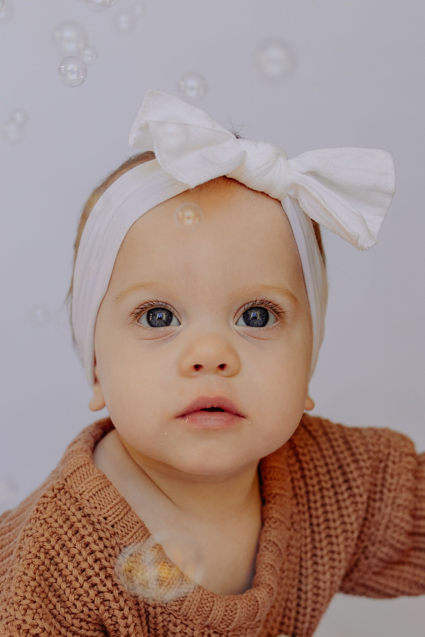 Sweet portrait of an infant wearing a white bow headband and knit sweater.