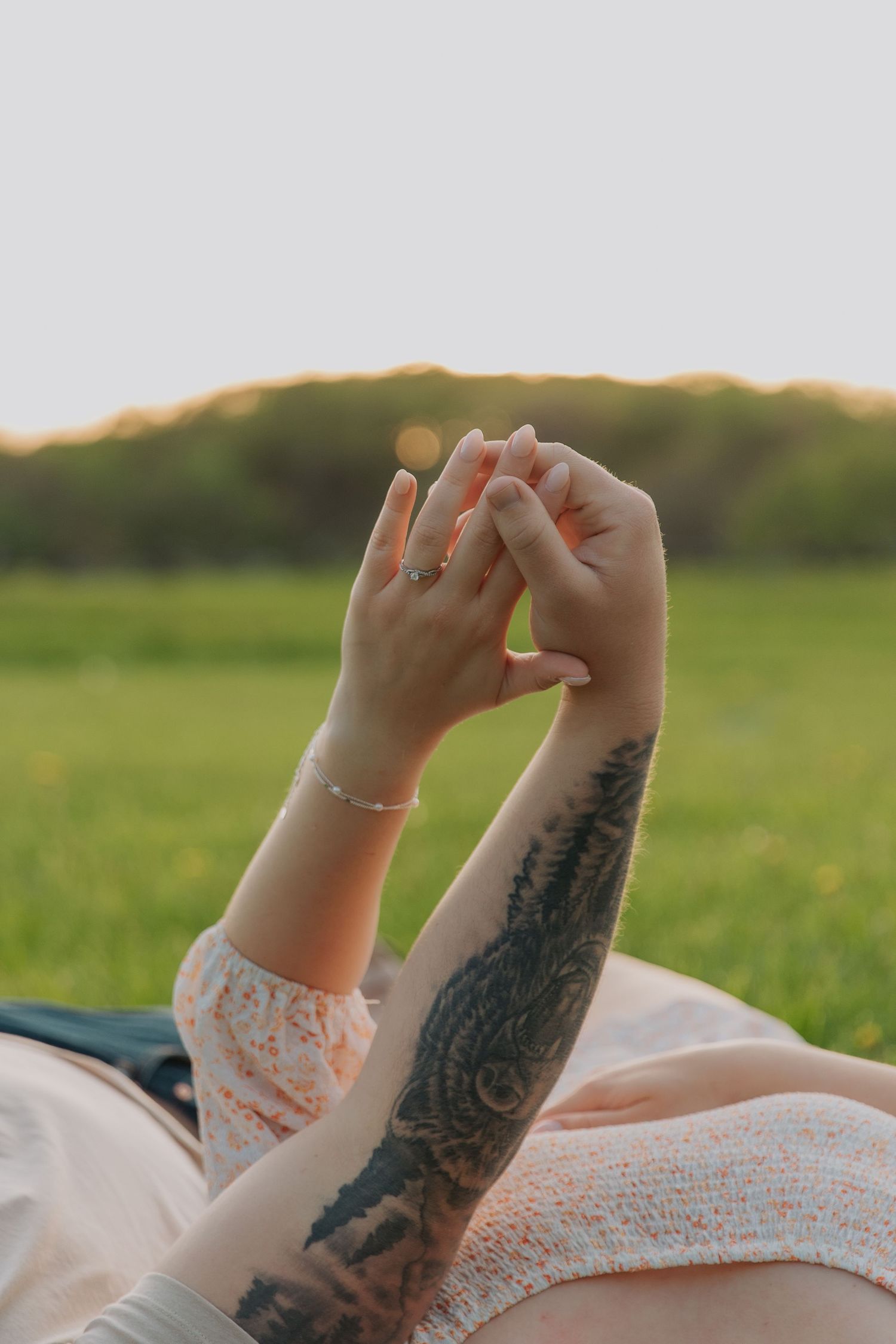 Close-up of interlocked hands with tattooed arms against a lace wedding dress.