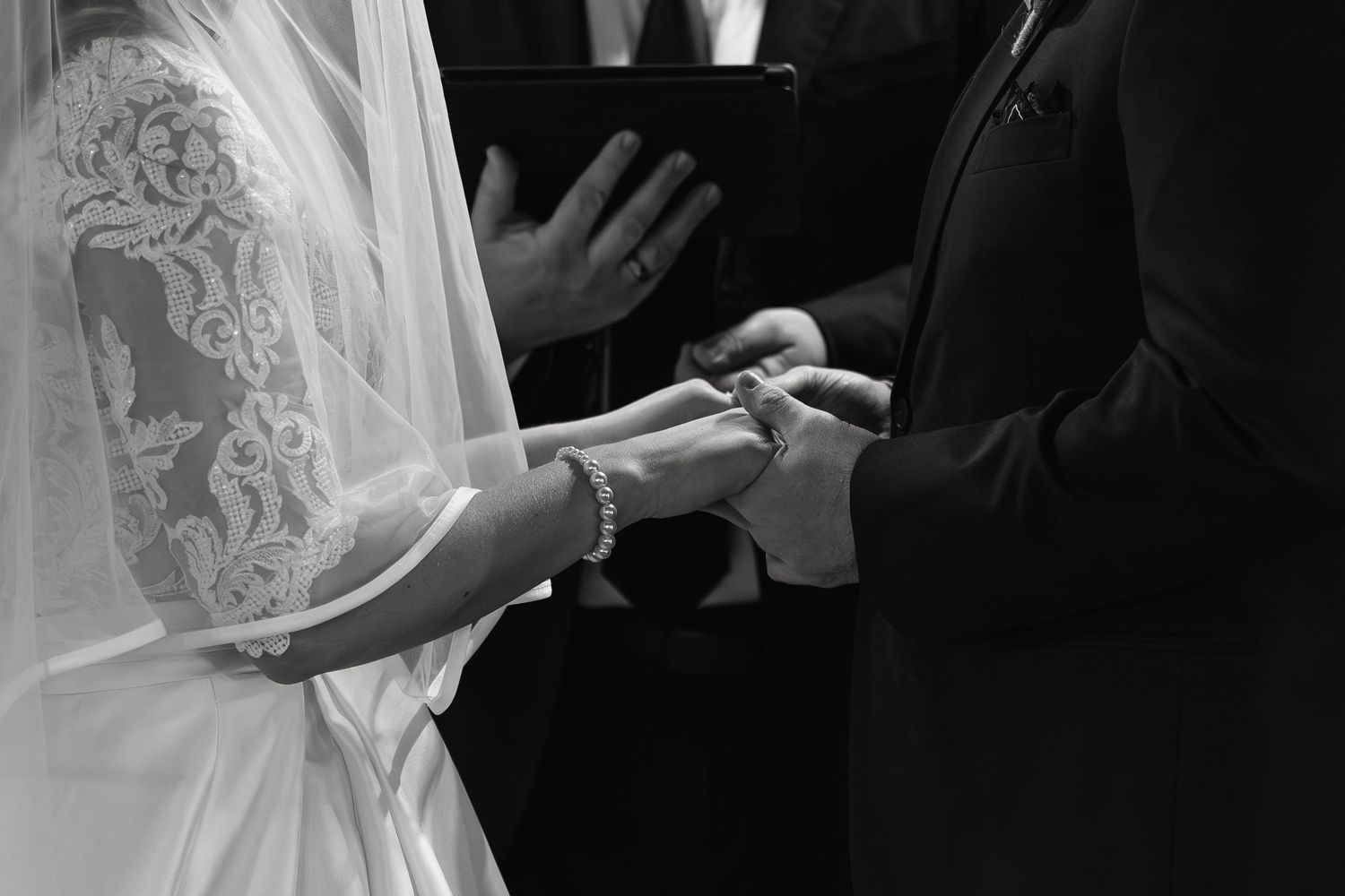 Black and white wedding photography showing elegant lace dress details and hands holding a bouquet.
