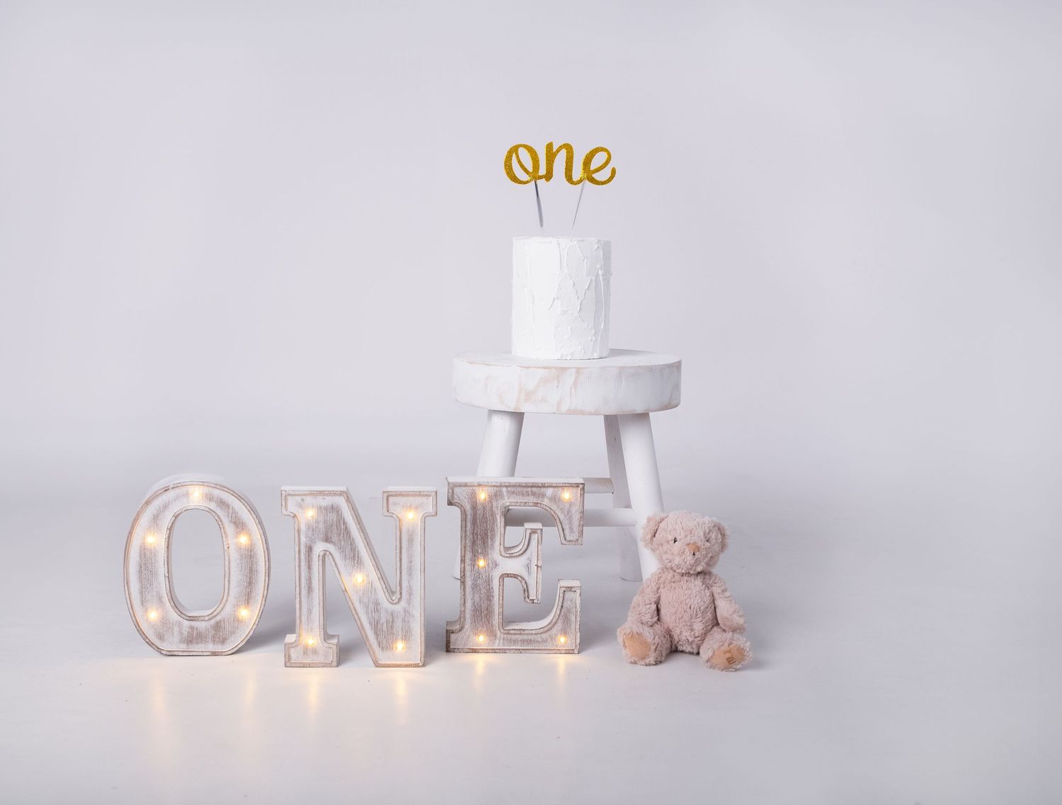 Gold 'ONE' letter decorations with teddy bears and white cake setup for first birthday.