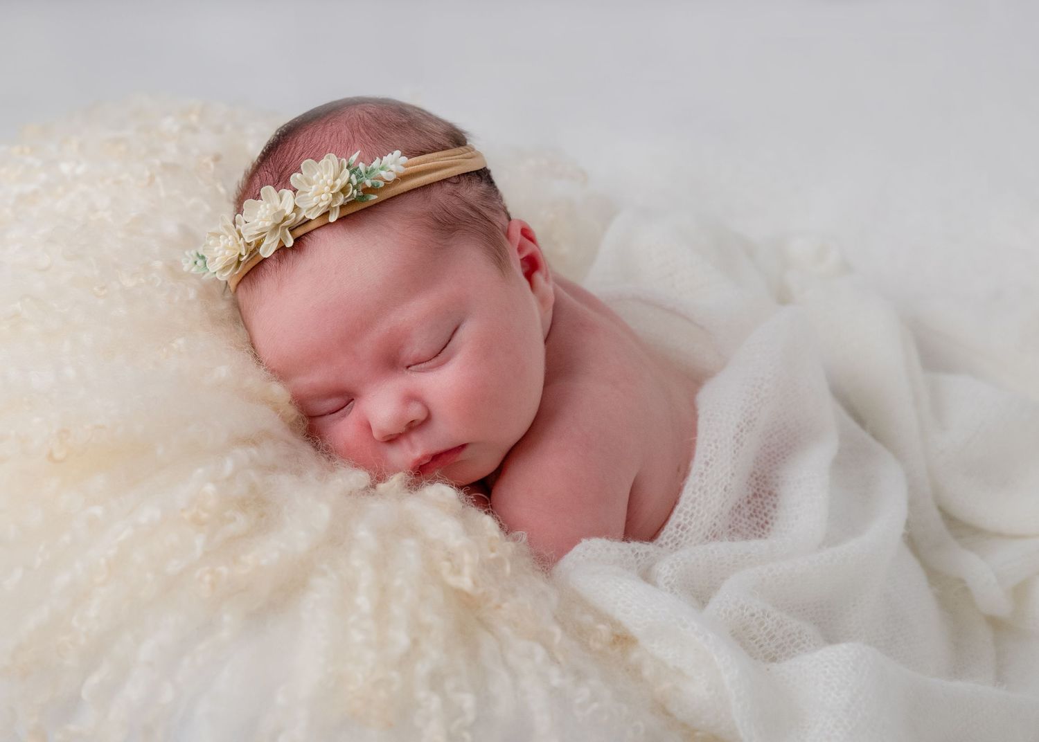 Peaceful newborn portraits with delicate white wraps and floral crown accessories.