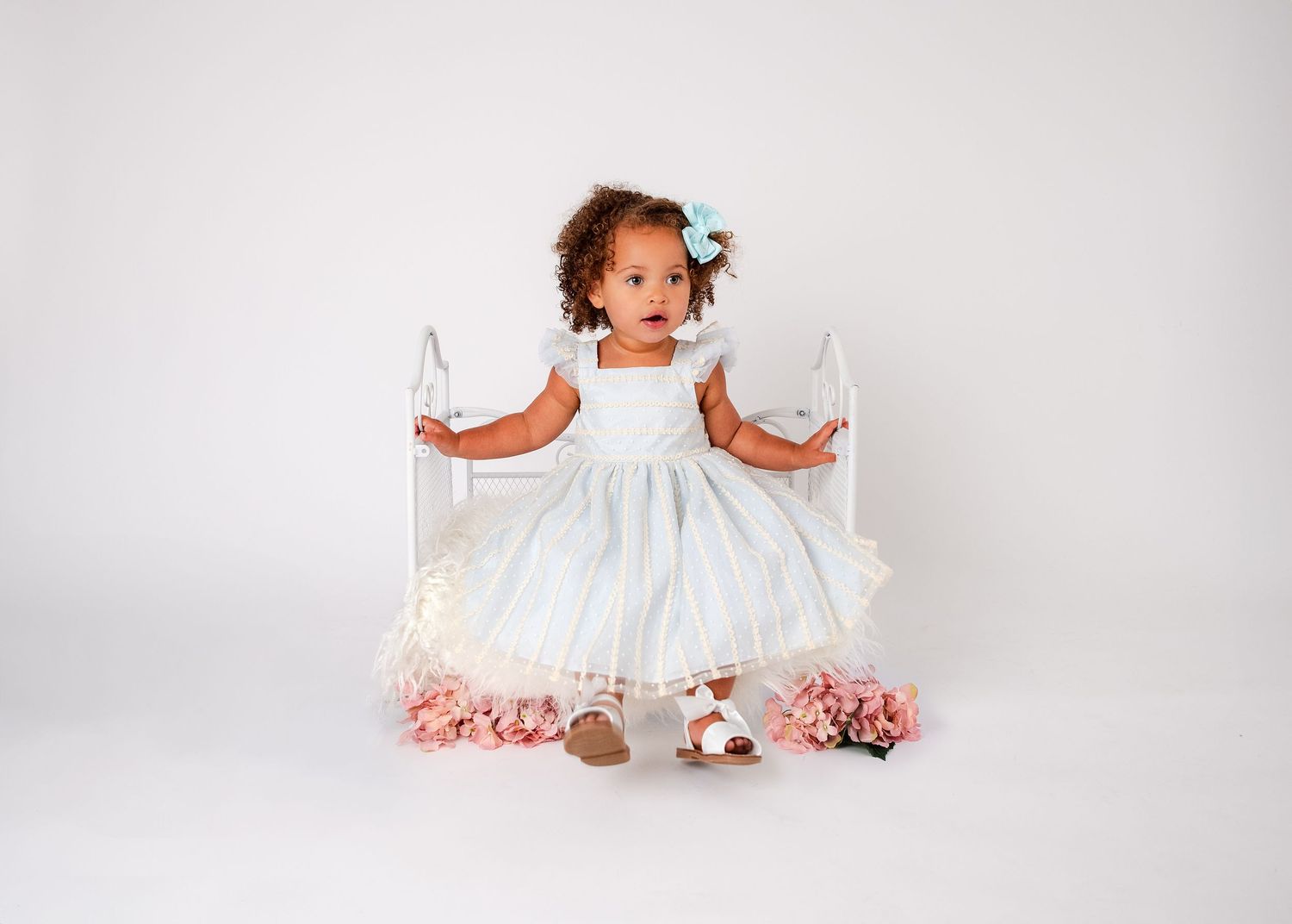 A child sits on the floor wearing a flowing white dress surrounded by delicate pink flowers.