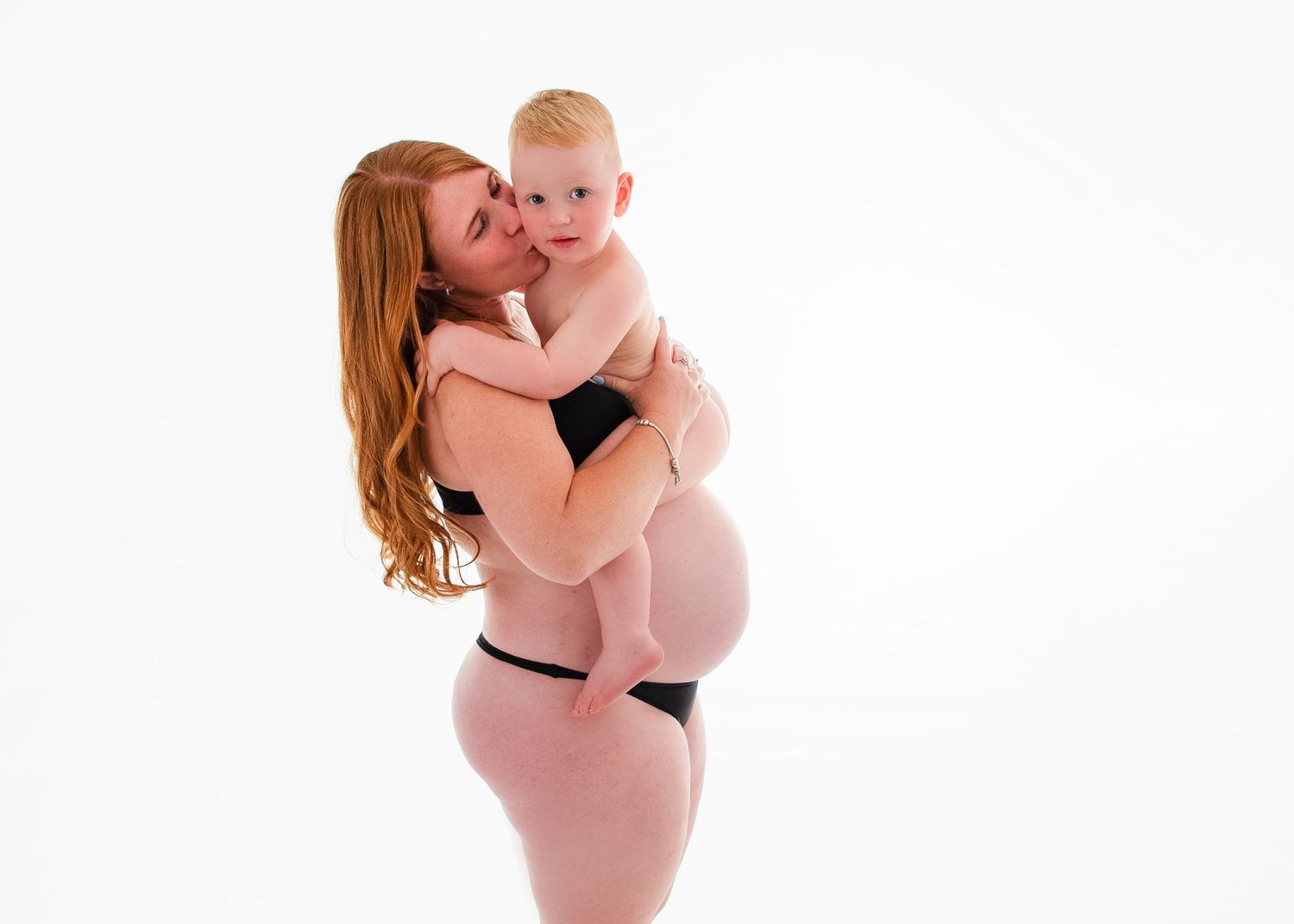 Intimate maternity photography session captured in white studio setting.