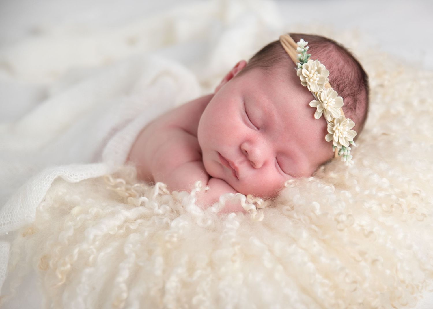 Newborn Photoshoot of Sleeping baby wearing a delicate lace headband lies peacefully on cream-colored textured blanket. Essex