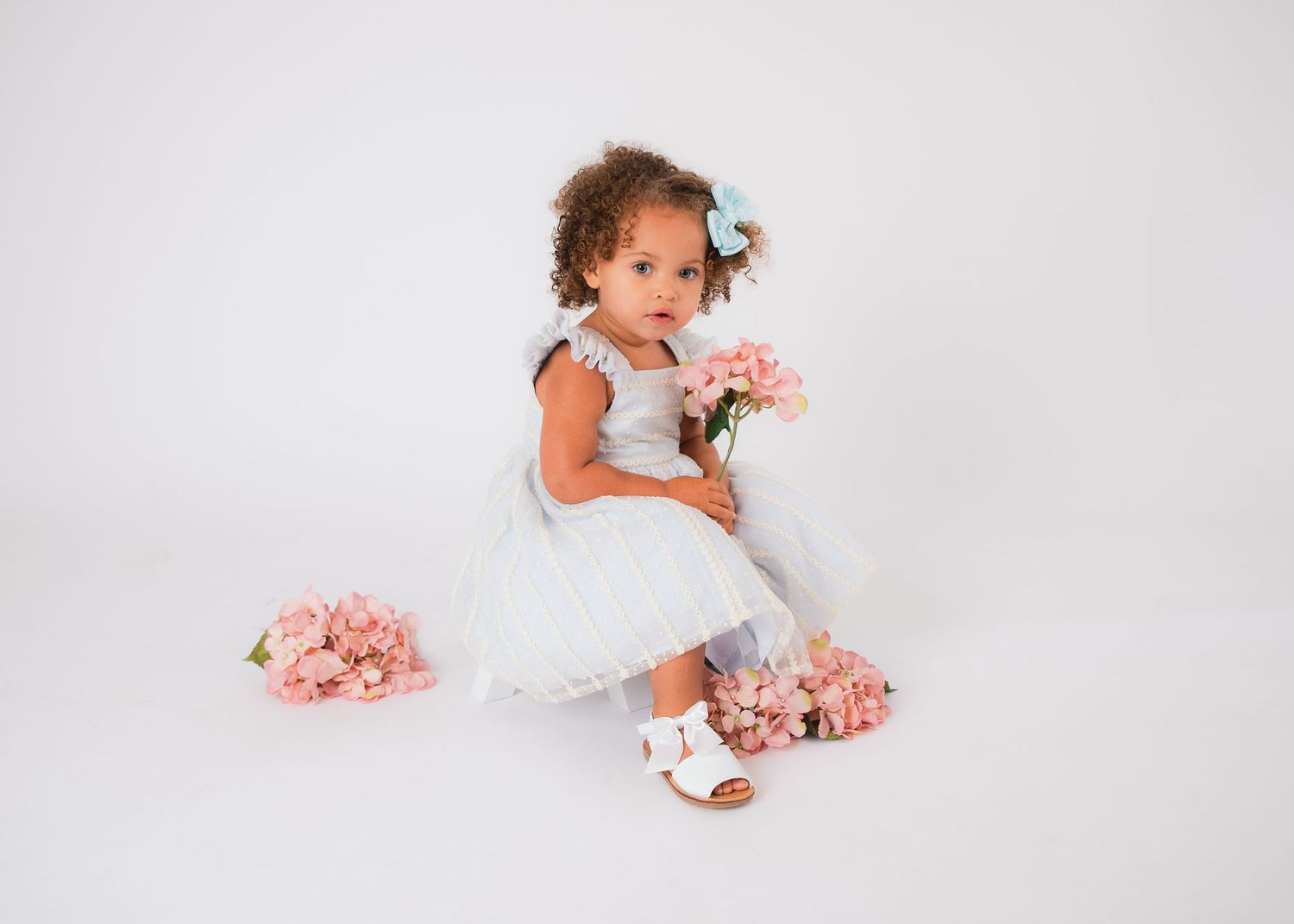 Clean white photography studio backdrop with scattered pink floral accents.