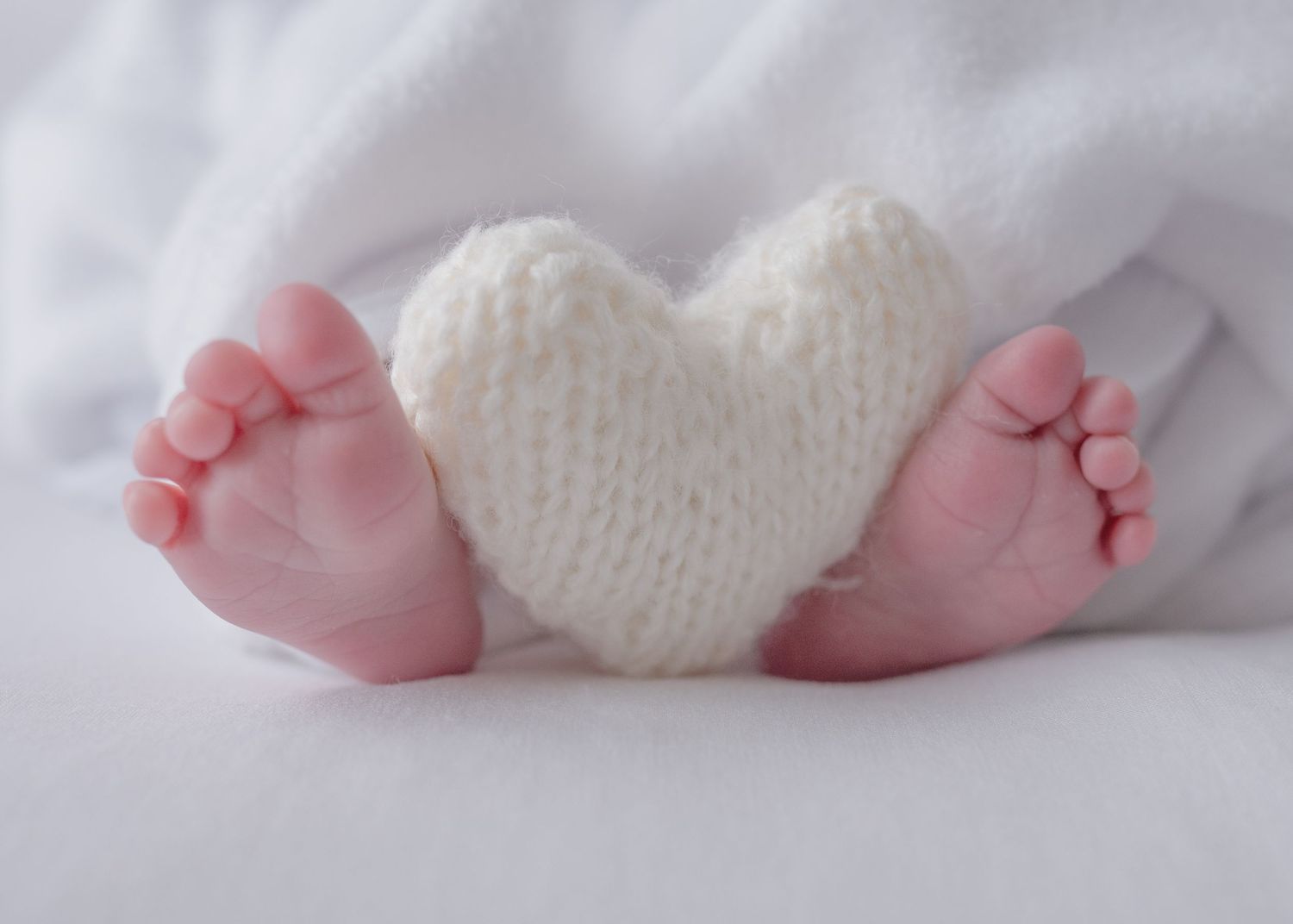 Tiny baby feet wearing white knit booties against soft white background.