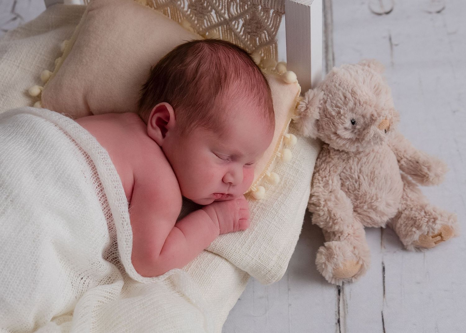 Newborn baby sleeping peacefully with a teddy bear on white blankets.