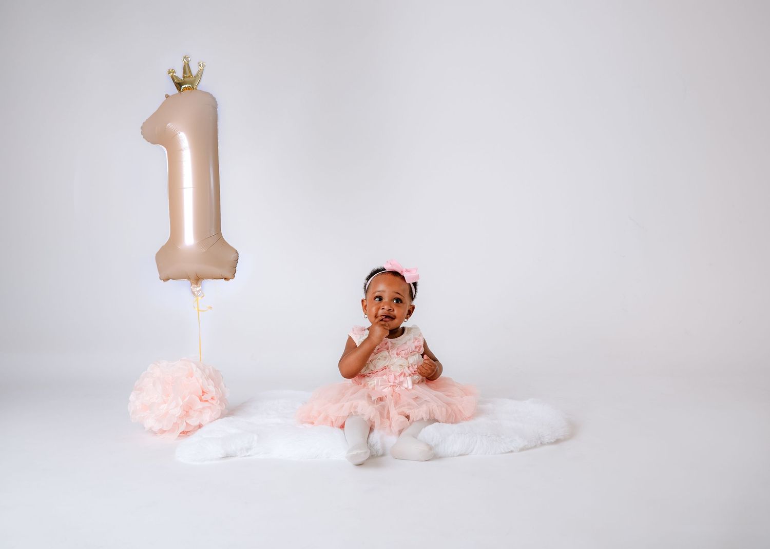 Pink themed first birthday photo setup with decorative crown and number one balloon.