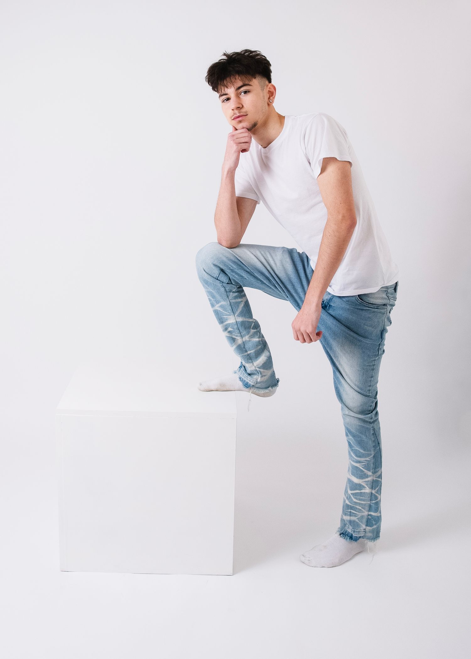 Fashion model demonstrates dynamic poses on white block wearing casual denim and white shirt.