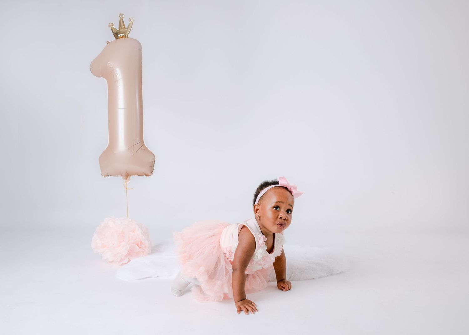 Birthday setup with pink number one balloon and crown against white backdrop.