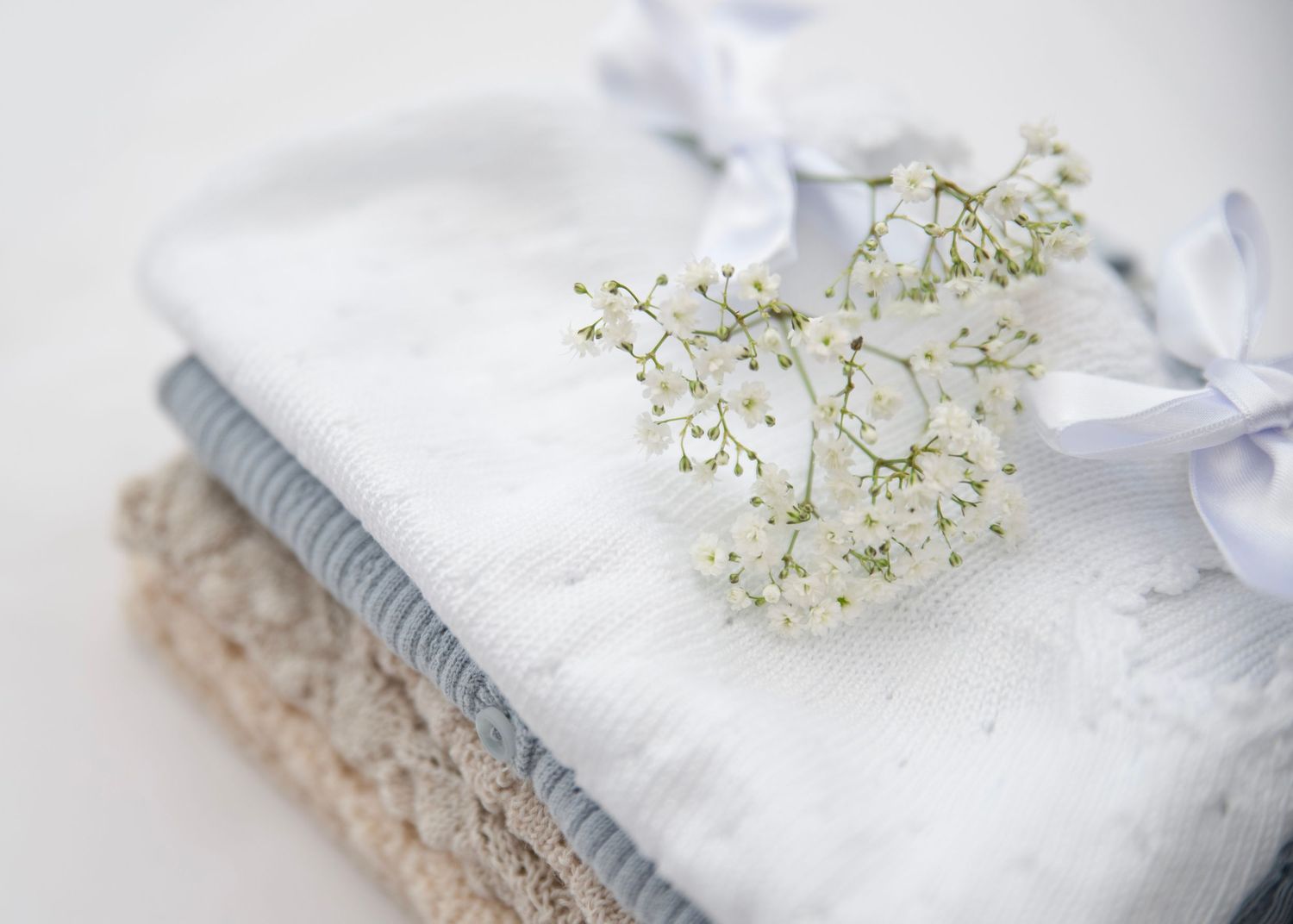 White baby's breath flowers laying on folded light gray and white textiles.