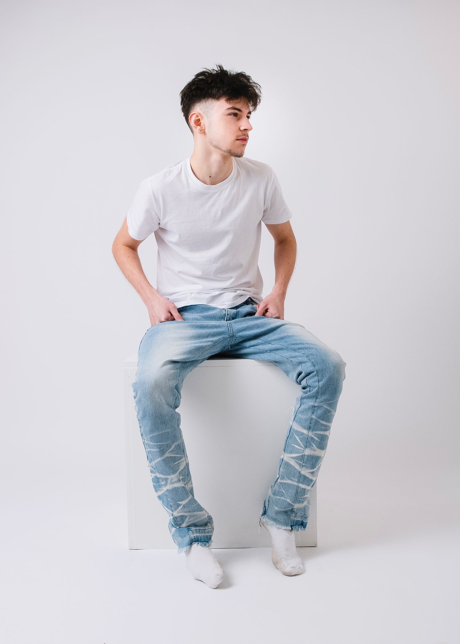 Urban fashion photograph features model in ripped jeans and white tee on minimalist set.